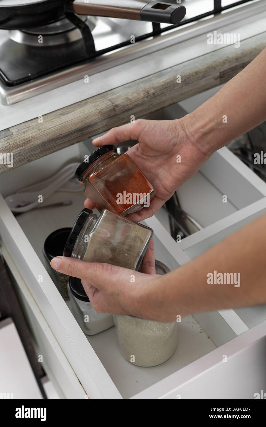 Die Hände einer Frau reichen in eine Küchenschublade, um Gewürzgläser in einer sauberen und organisierten modernen Speisekammer herauszunehmen. Stockfoto