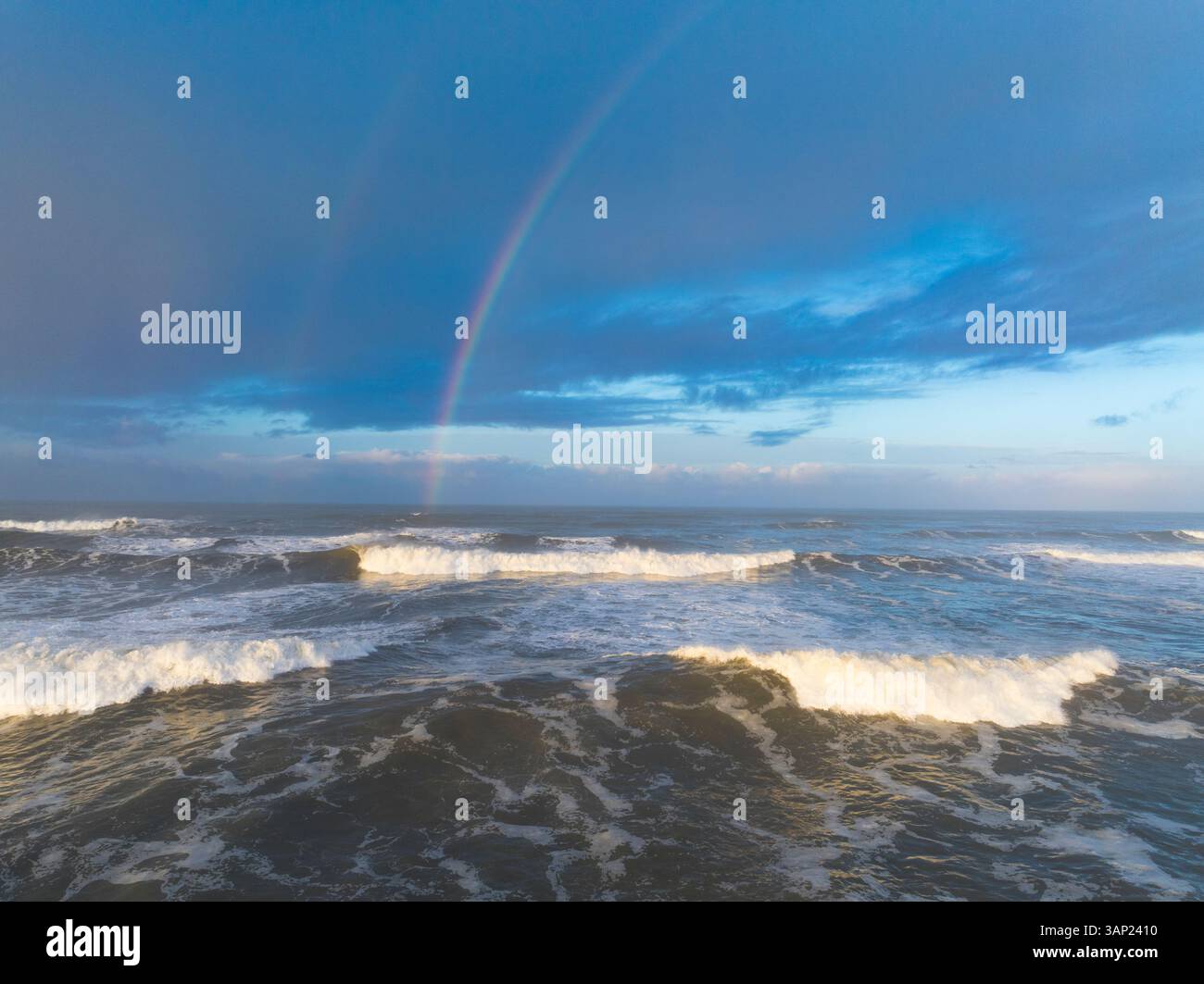 Aus der Vogelperspektive auf einen ruhigen Sonnenaufgang über Mocrocks Beach mit einem farbenfrohen Regenbogen und Surfen auf dem Pazifik, Pacific Beach, Washington, USA. Stockfoto