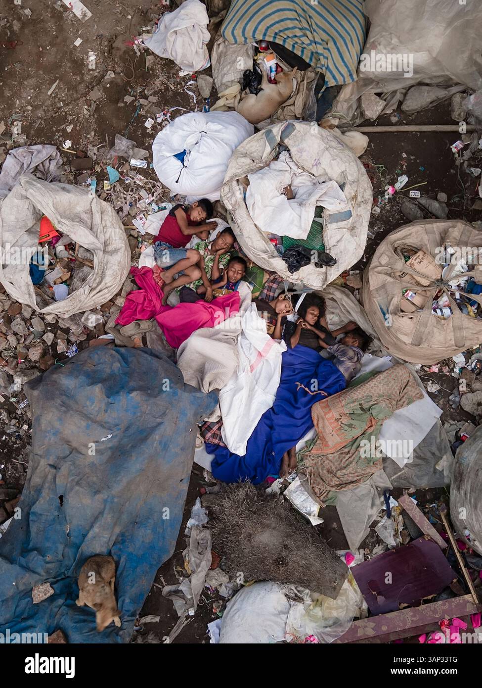 Dhaka, Bangladesch - 27. März 2023: Aus der Vogelperspektive von Kindern, die auf provisorischen Betten zwischen Plastikmüll und Müll in einer überfüllten städtischen Umgebung schlafen; Stockfoto