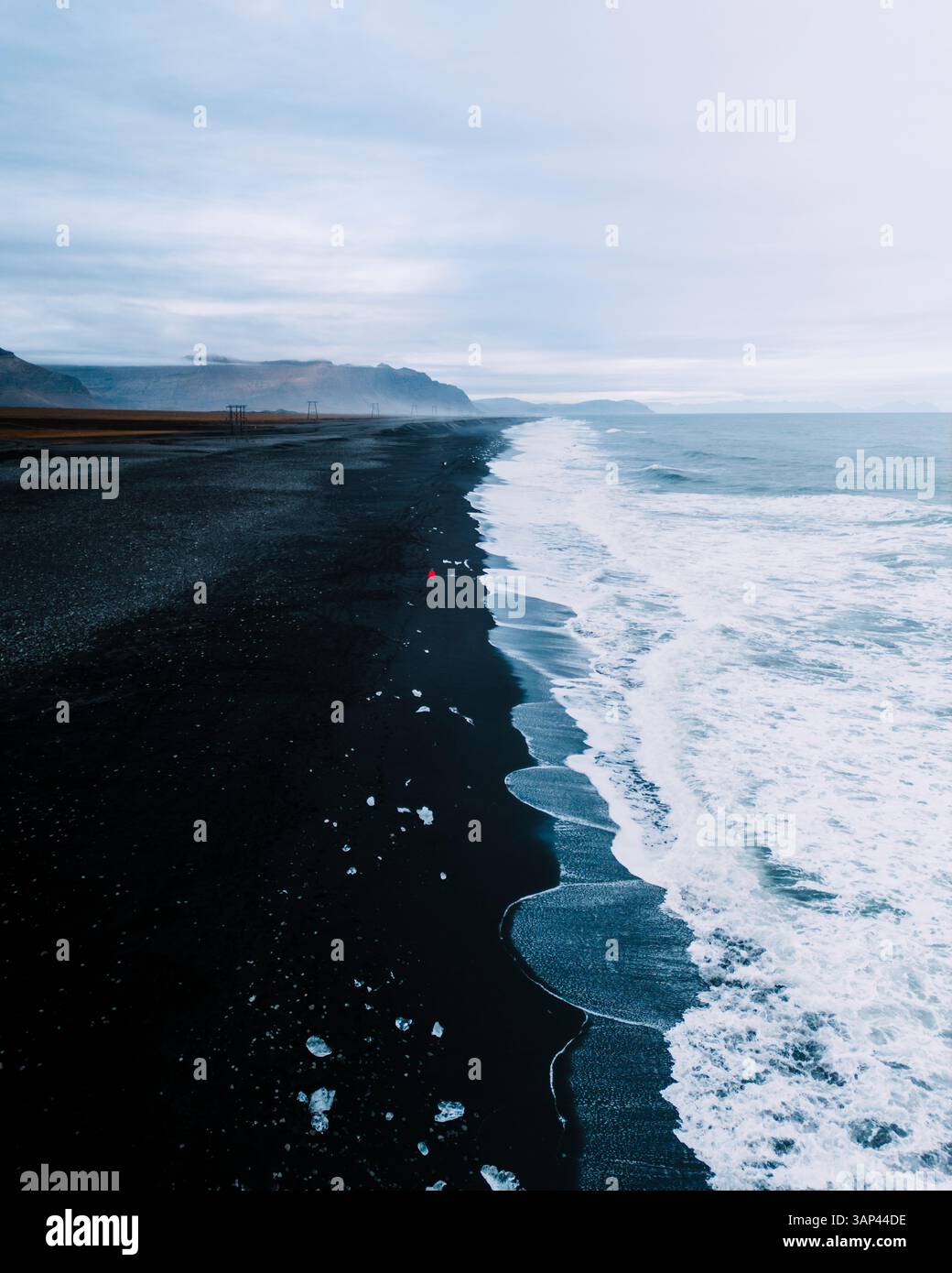 Drohnenblick auf Diamond Beach mit einer Person in roter Jacke, schwarzem Sand und Eisfelsen am Strand, Südosten Islands. Stockfoto