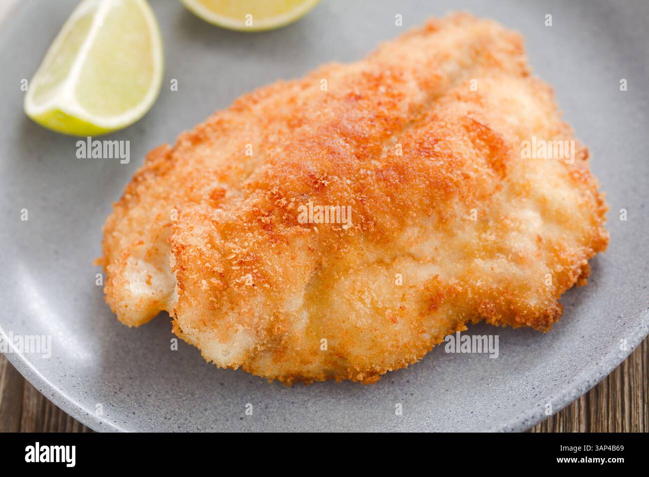 Gebratenes paniertes Jack-Filet auf blauer Platte mit Zitronenscheiben (selektiver Fokus, Fokus auf die Vorderseite des Fisches) Stockfoto