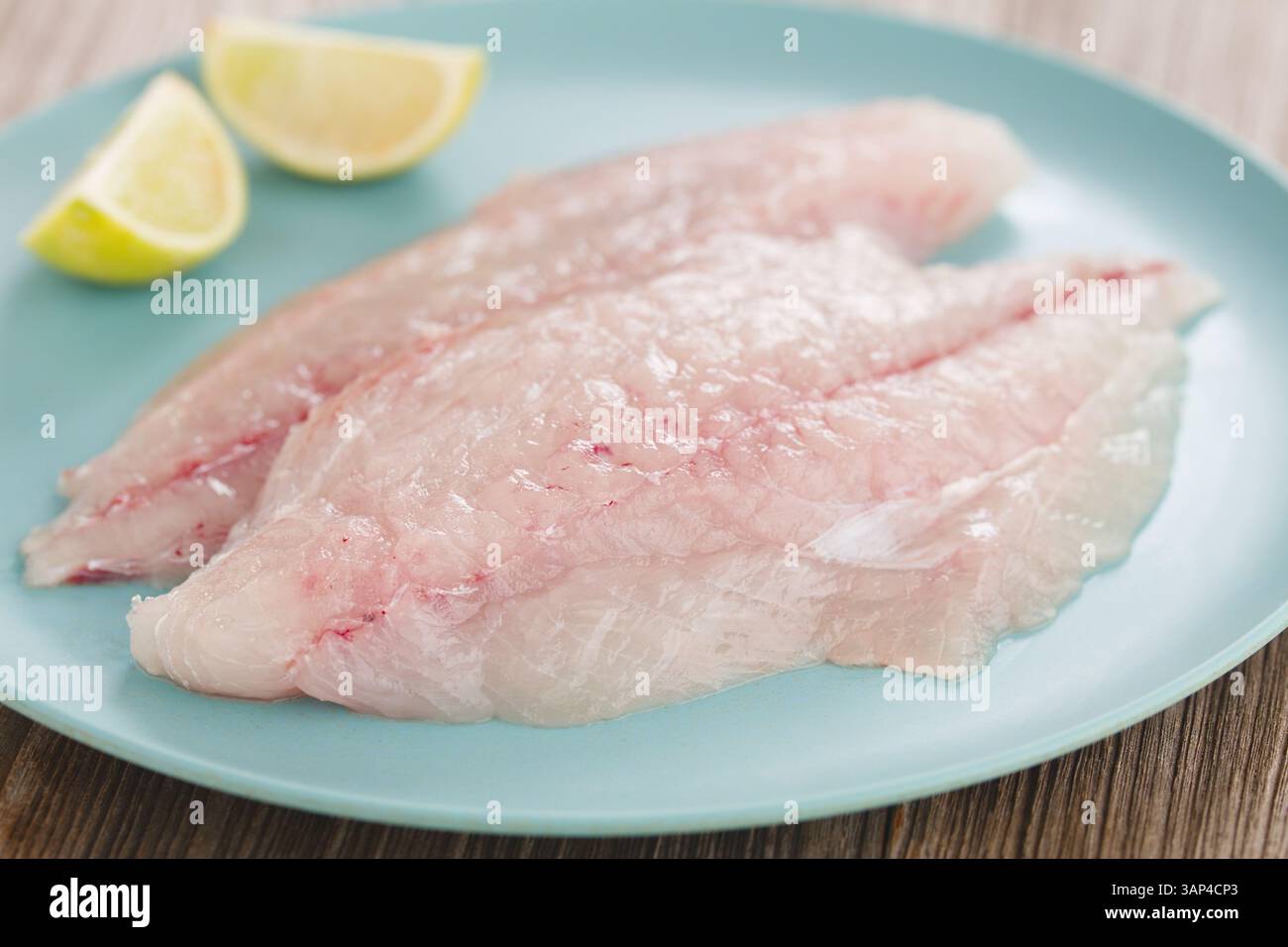 Frische, rohe Jack-Fischfilets auf blauer Platte mit Zitrone (selektiver Fokus, Fokus auf die Vorderseite des Fisches) Stockfoto