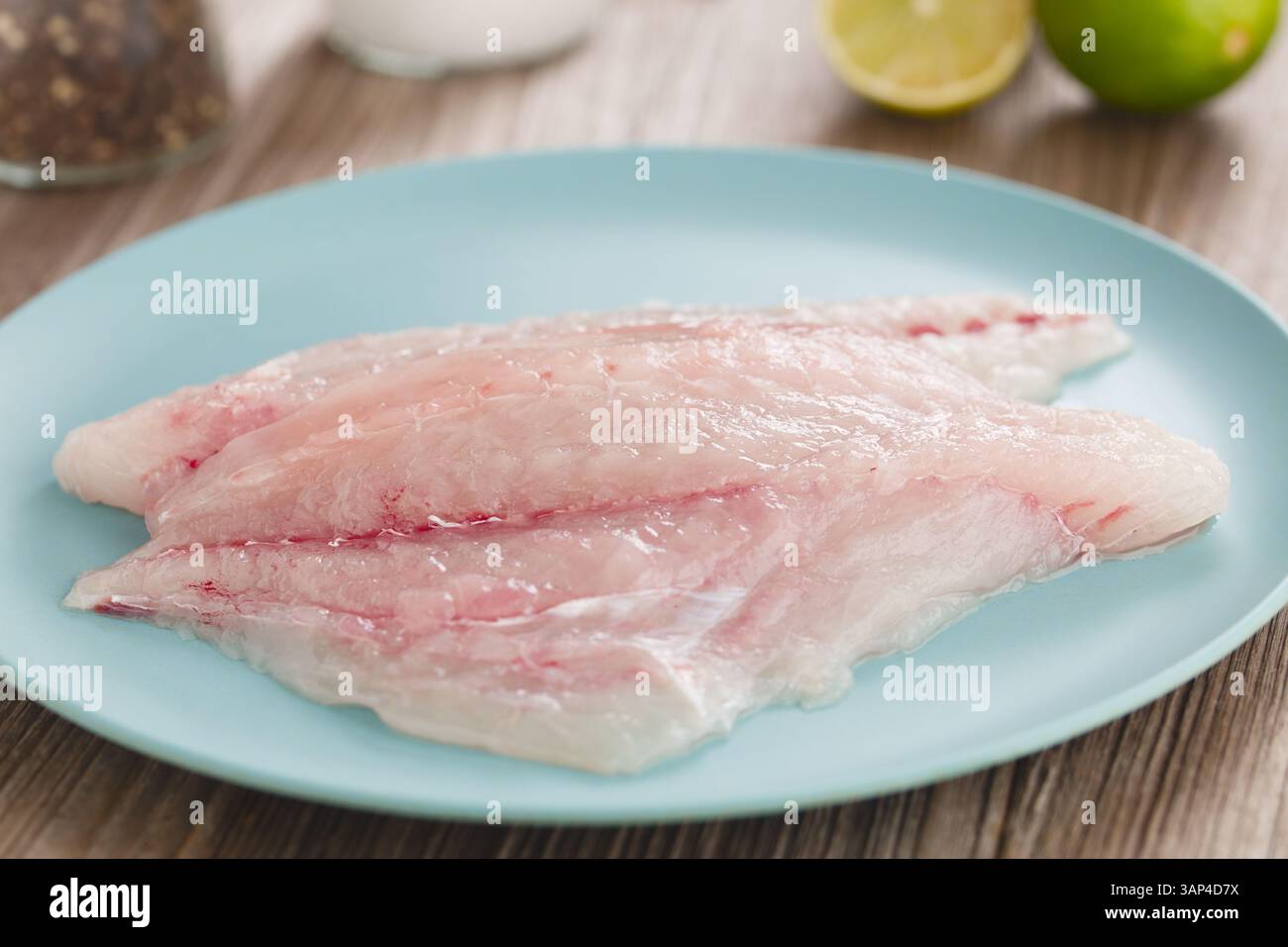 Frische, rohe Jack-Fischfilets auf blauer Platte, Salz, Pfeffer und Limetten im Rücken (selektiver Fokus, Fokus entlang der Mitte des Fisches) Stockfoto