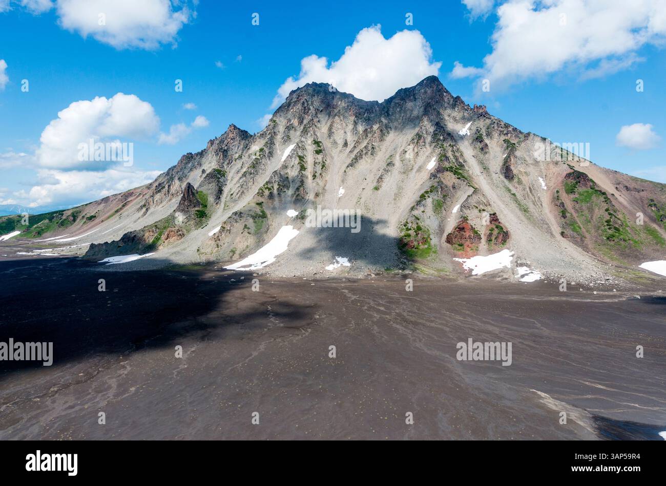 Aus der Vogelperspektive auf den Vulkan gorely, umgeben von felsigem Gelände und schneebedeckten Gipfeln unter bewölktem Himmel, Kamtschatka Halbinsel, Russland. Stockfoto