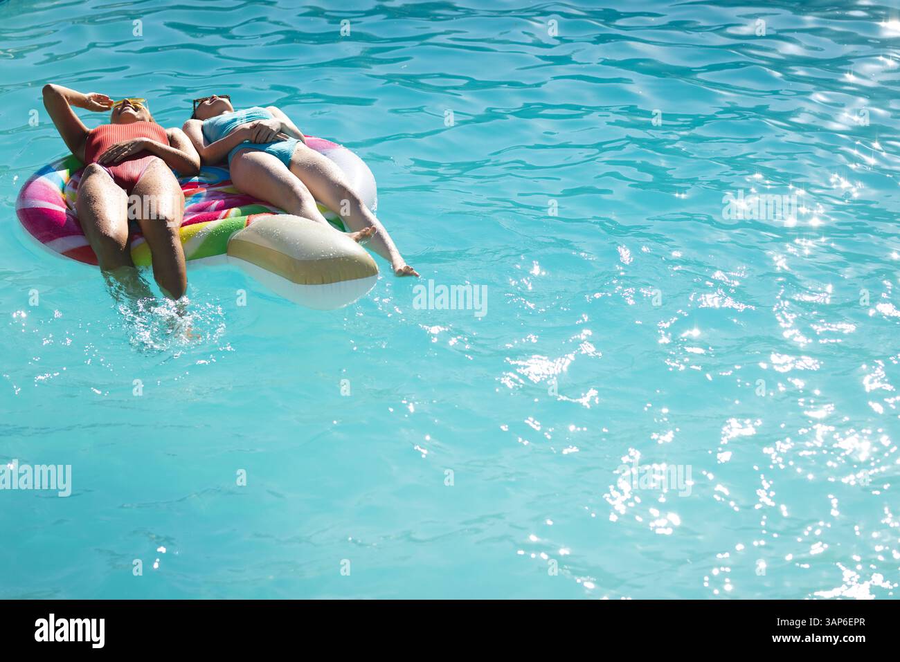 Verschiedene Freunde, die sich auf bunten Eiskegel entspannen, schweben im blauen Außenpool unter strahlender Sonne, Polizist Stockfoto