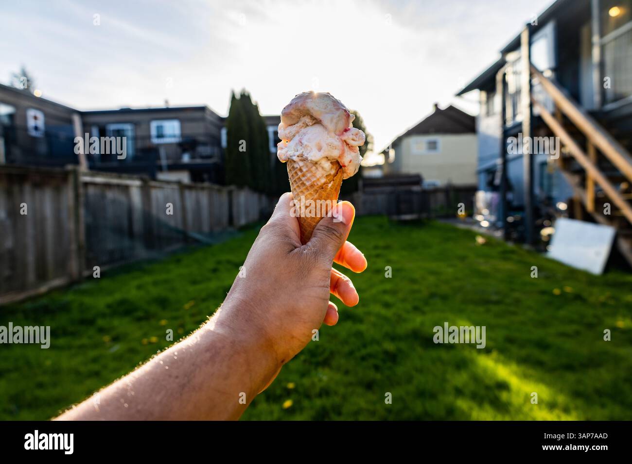 Die Hand hält Erdbeereiskegel im Hinterhof mit der Sonne hinter dem Kegel Stockfoto