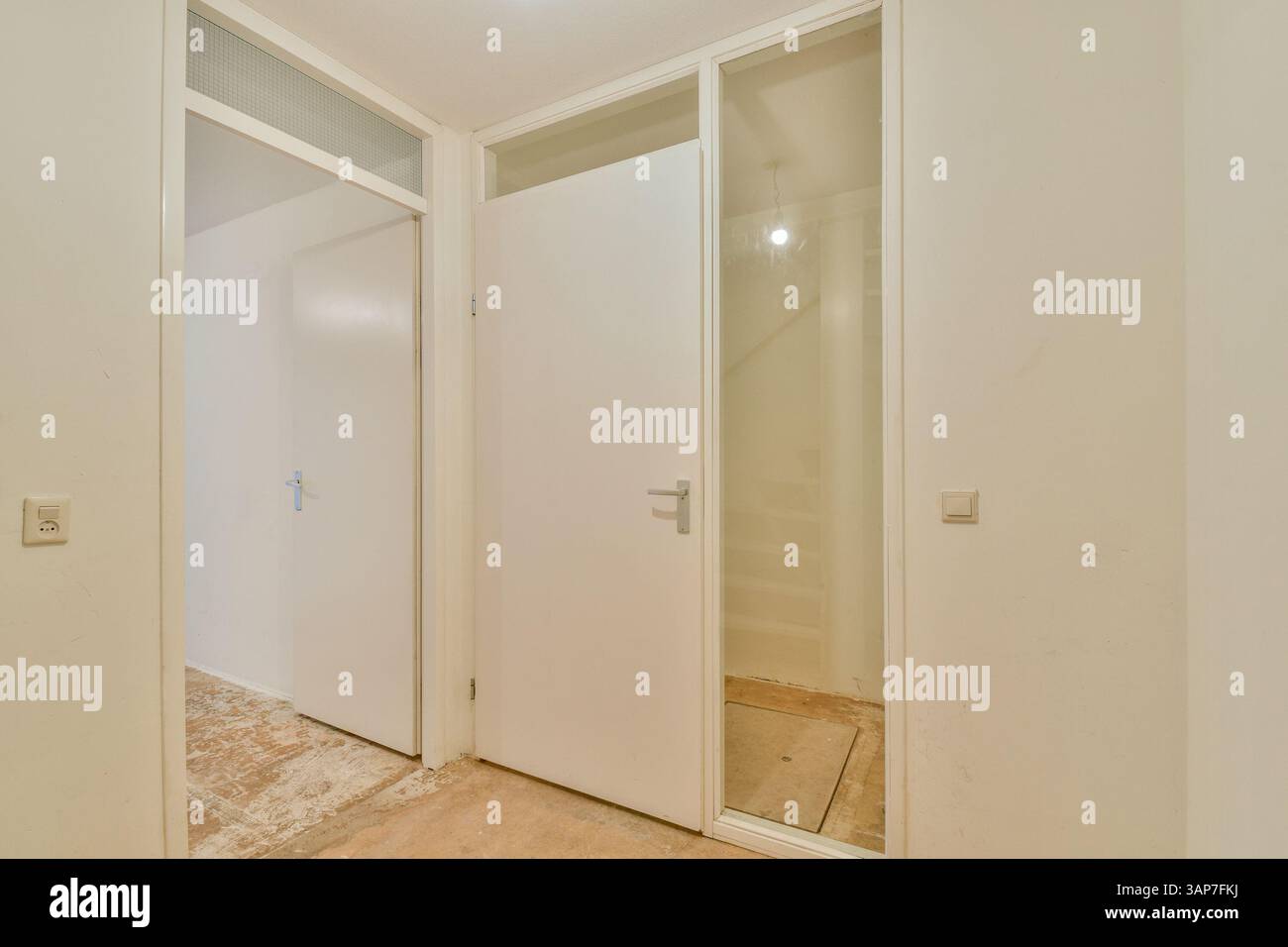 Ein sauberer und minimalistischer Innenkorridor mit weißen Wänden, eleganten Türen und einer dezenten dekorativen Note der Beleuchtung sorgt für eine offene und luftige Atmosphäre. Stockfoto