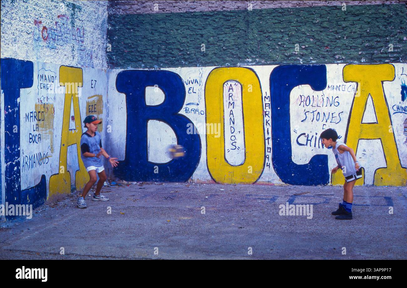 Argentinien, Buenos Aires - Kinder spielen Fußball im Viertel La Boca mit einem Wandbild des Fußballvereins La Boca Juniors. Stockfoto