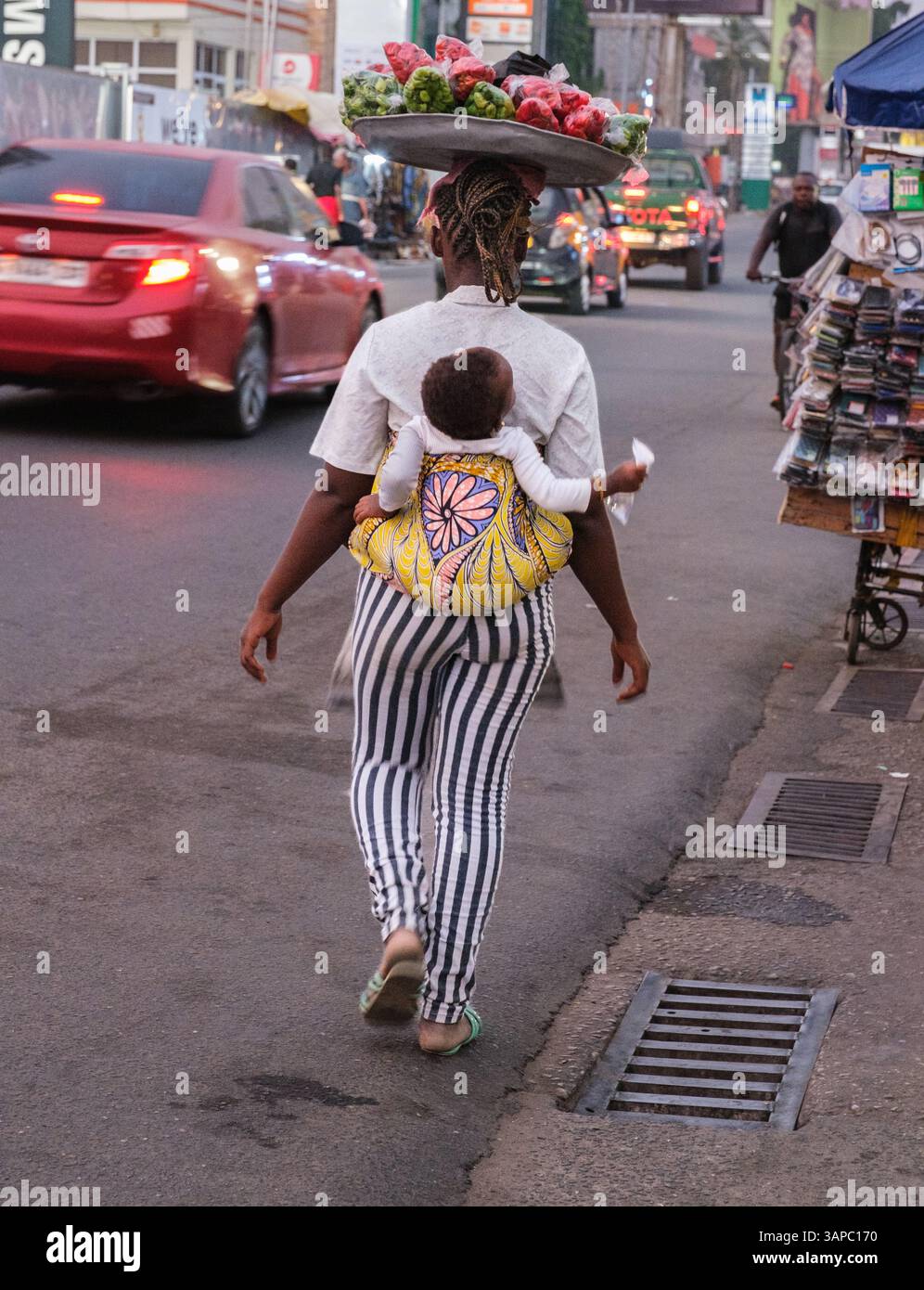 Accra, Ghana. Oxford Street Scene. Frau trägt Baby auf dem Rücken, Tablett mit Paprika in Taschen auf dem Kopf. Stockfoto