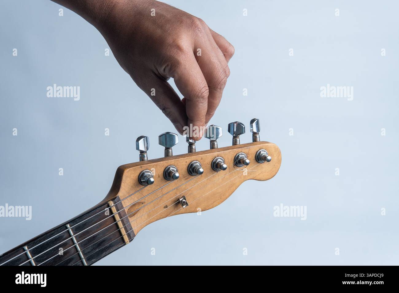 Nahaufnahme einer Hand, die Stimmstifte auf einer elektrischen Gitarre einstellt, isoliert auf weißem Hintergrund. Stockfoto