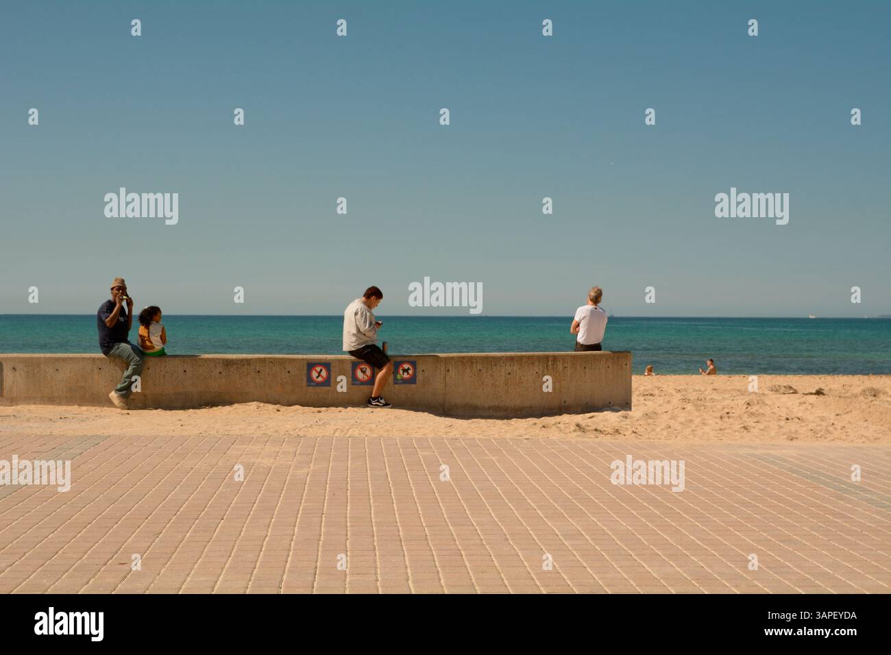 Menschen, die an der Meeresmauer neben der Bucht von Palma bei Les Meravelles, Insel Mallorca, Spanien, sitzen, Stockfoto