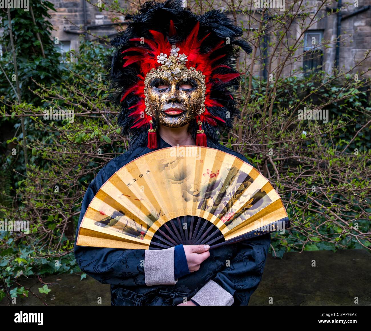 Ein Mann mit chinesischem Kostüm und Fan und venezianischer Maske für das Granatapfelfestival, Scottish Storytelling Centre, Edinburgh, Schottland, Großbritannien Stockfoto