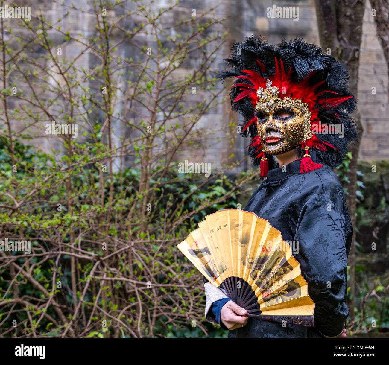 Ein Mann mit chinesischem Kostüm und Fan und venezianischer Maske für das Granatapfelfestival, Scottish Storytelling Centre, Edinburgh, Schottland, Großbritannien Stockfoto