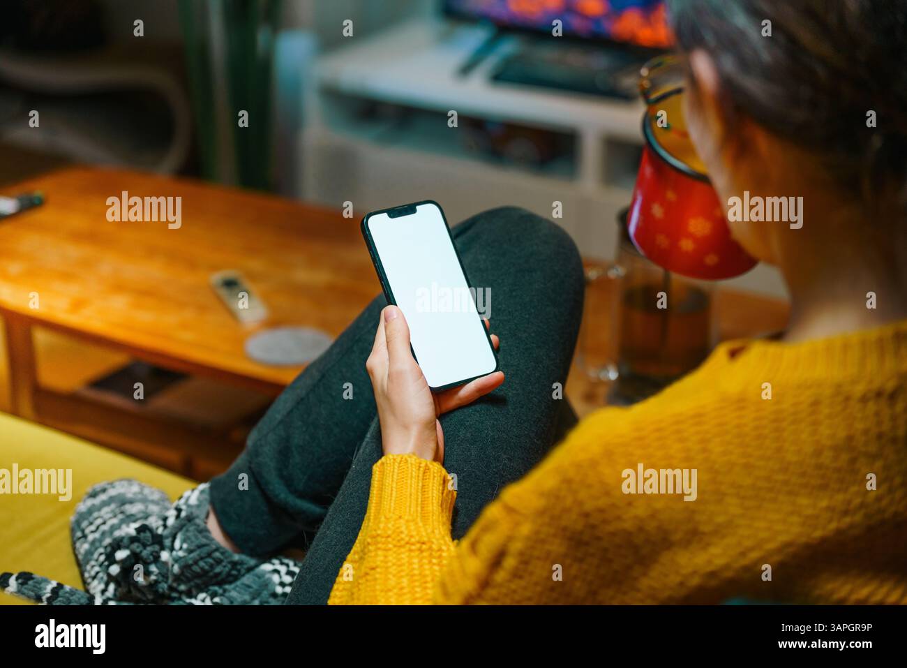 Warme Wohnatmosphäre mit Frau, die ihr Smartphone benutzt, während sie am Kamin entspannt, Winterstimmung Stockfoto