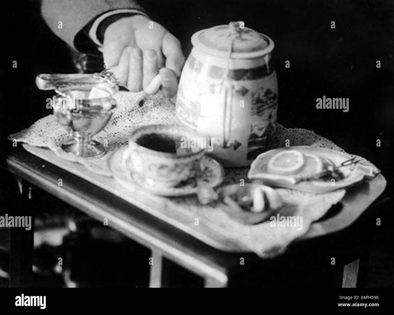 Dieses Foto fängt die Hände von John Jacob Niles ein, der für seine Beiträge zur Musik und zum Volksgesang bekannt ist, während er Tee serviert. Das Bild hebt einen ruhigen, persönlichen Moment hervor, der sowohl seine Identität als auch den kulturellen Kontext der Zeit widerspiegelt. Stockfoto