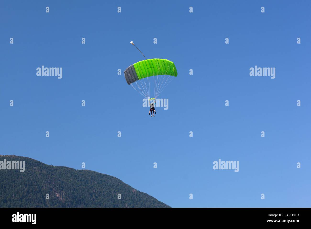 Ein Gleitschirm mit grünem Fallschirm fährt hinunter nach Kanin, Slowenien, mit blauem Himmel im Hintergrund. Stockfoto