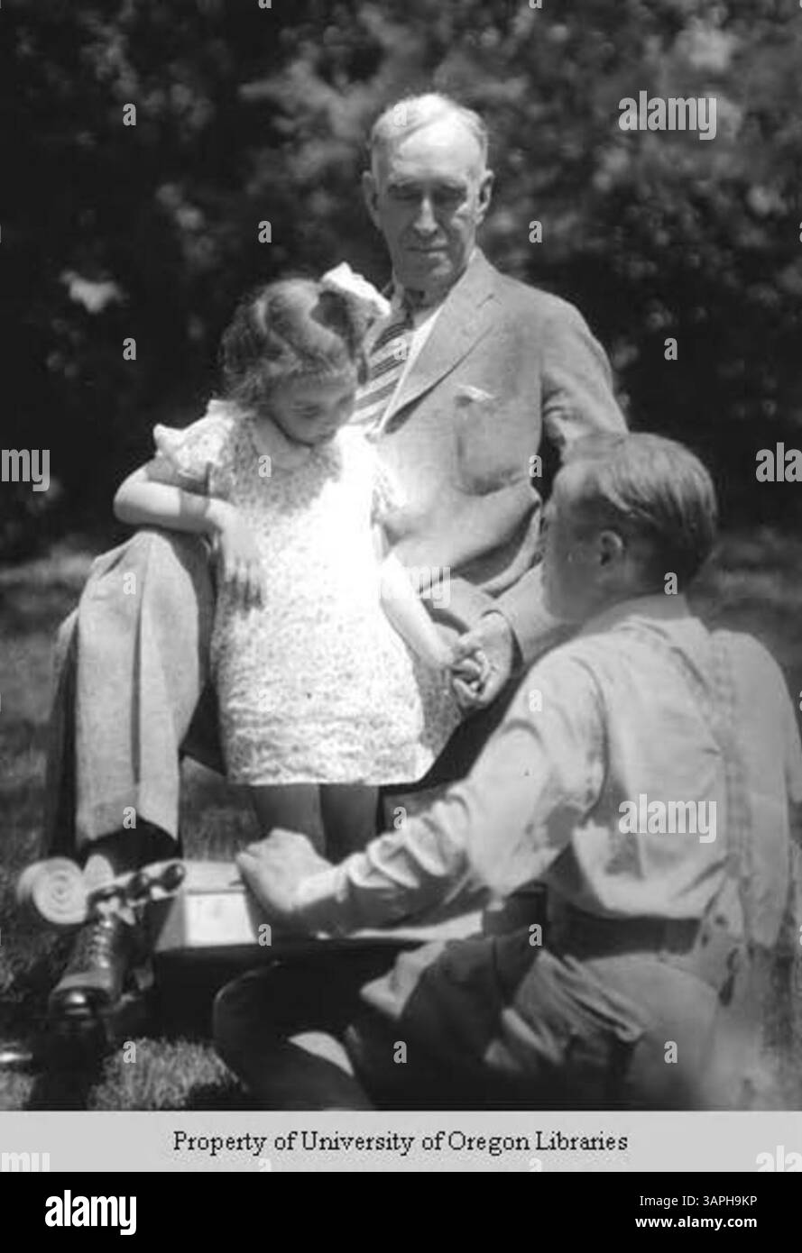 Frank Leonard McVey ist mit seiner Enkelin und John Jacob Niles auf einem Foto aus der Sammlung der University of Oregon Libraries abgebildet. Das Bild fängt einen Moment mit zwei bedeutenden Persönlichkeiten auf dem Gebiet der Musik und der Wissenschaft ein, wobei McVey Präsident der Universität und Niles ein bekannter amerikanischer Folk-Musiker ist. Stockfoto