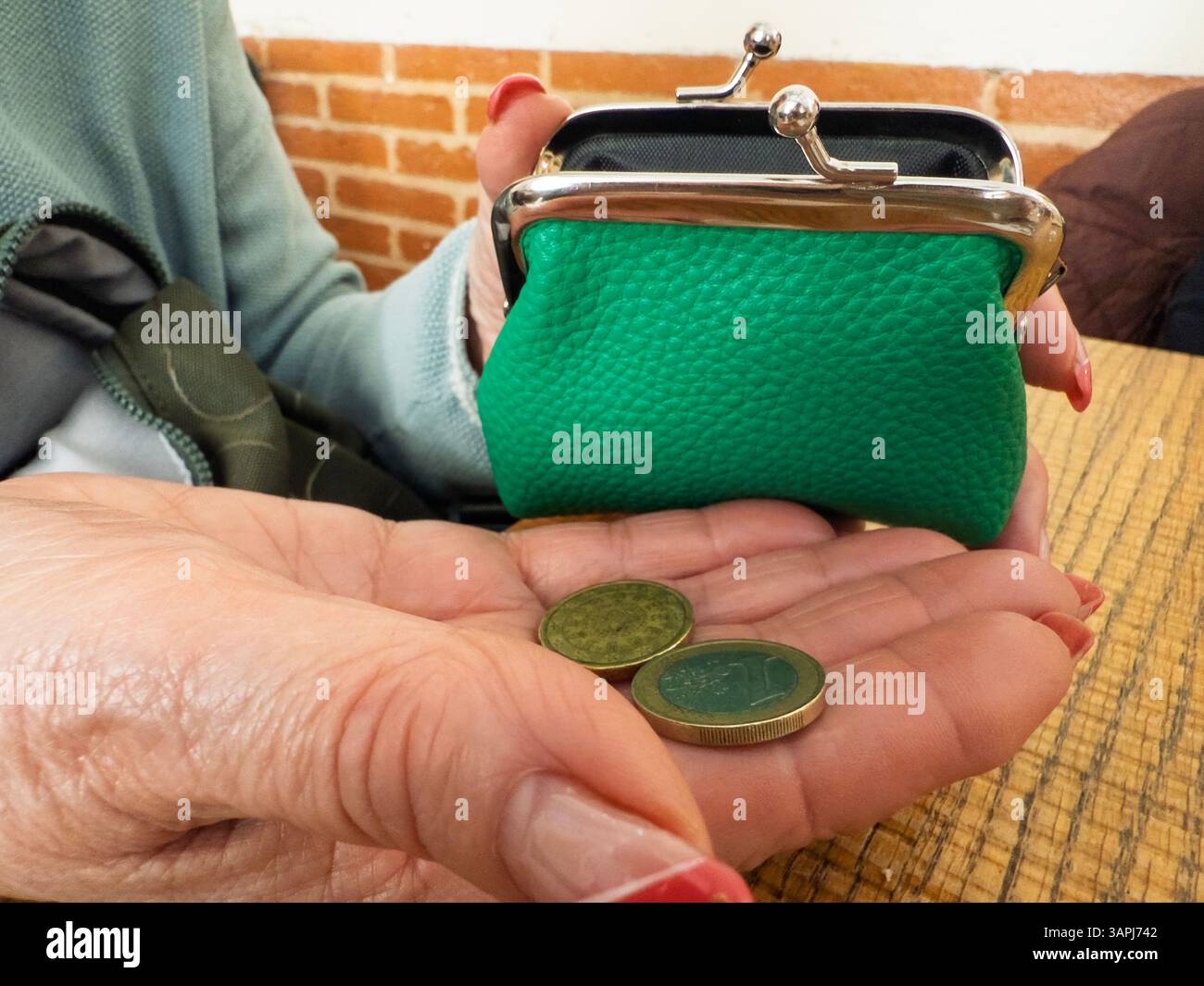 Eine ältere Frau zählt die verbleibenden Münzen aus ihrer leeren Tasche, was finanzielle Not und steigende Lebenshaltungskosten veranschaulicht Stockfoto