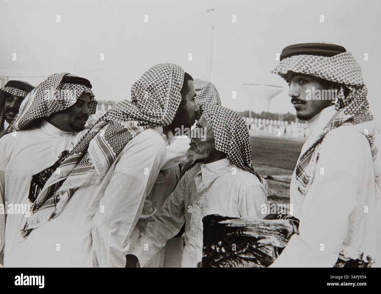 Saudi-arabischer Mann, der traditionelle Kleidung trägt, küsst die Stirn eines älteren Mannes und grüßt einander Stockfoto