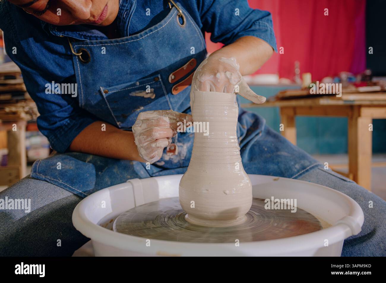 Nahaufnahme der Hände einer Latina, die in ihrer Werkstatt ein Keramikstück Formen. Das Bild erfasst Aufwand, Fokus und handgefertigte Details. Stockfoto