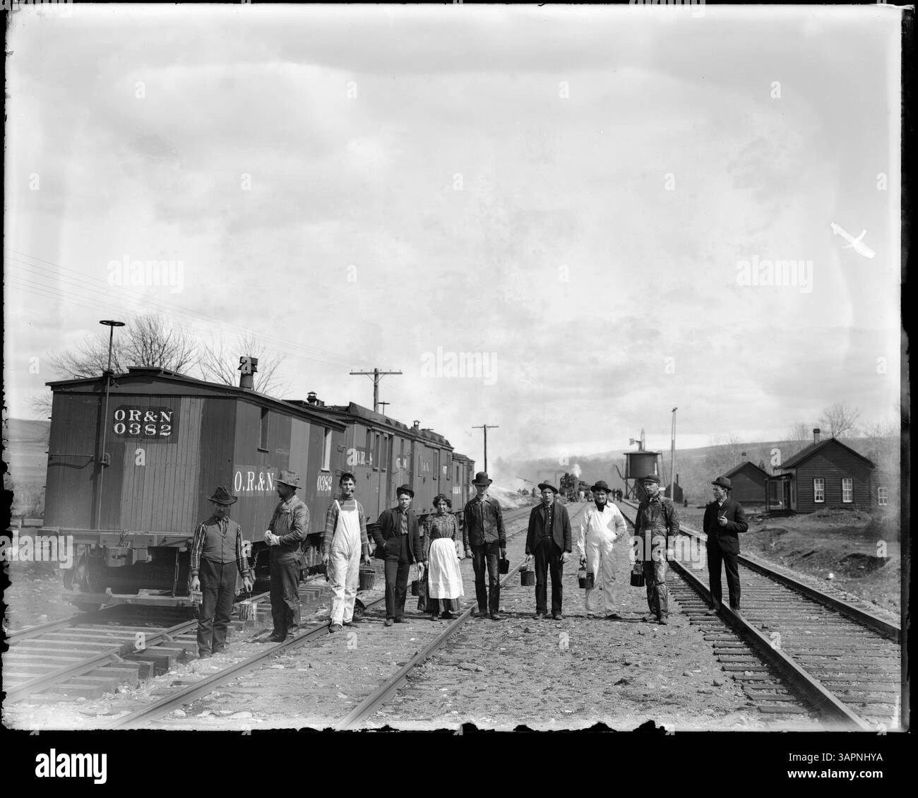Eine Fotografie (PH036 6771) von Lee Moorhouse, die OR&N-Autos zeigt, wobei Männer und Frauen mit Eimern und Pinseln auf Schienen arbeiten. Das Bild ist eine historische Dokumentation der Arbeit an der Eisenbahn in Oregon. Stockfoto