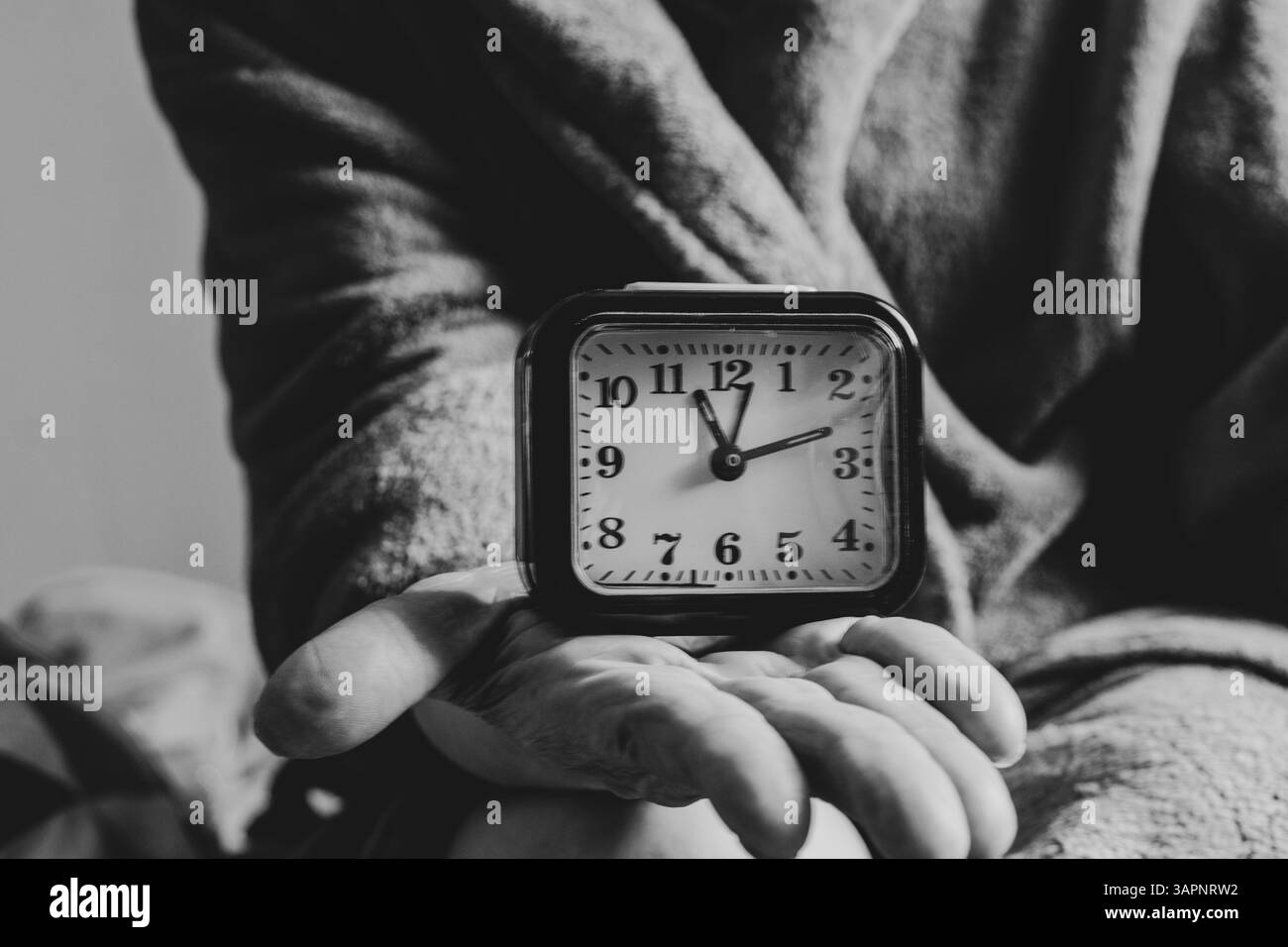 Eine ältere Frau hält zu Hause eine Tischuhr an der Hand, die Zeit läuft aus, das Leben ist flüchtig Stockfoto