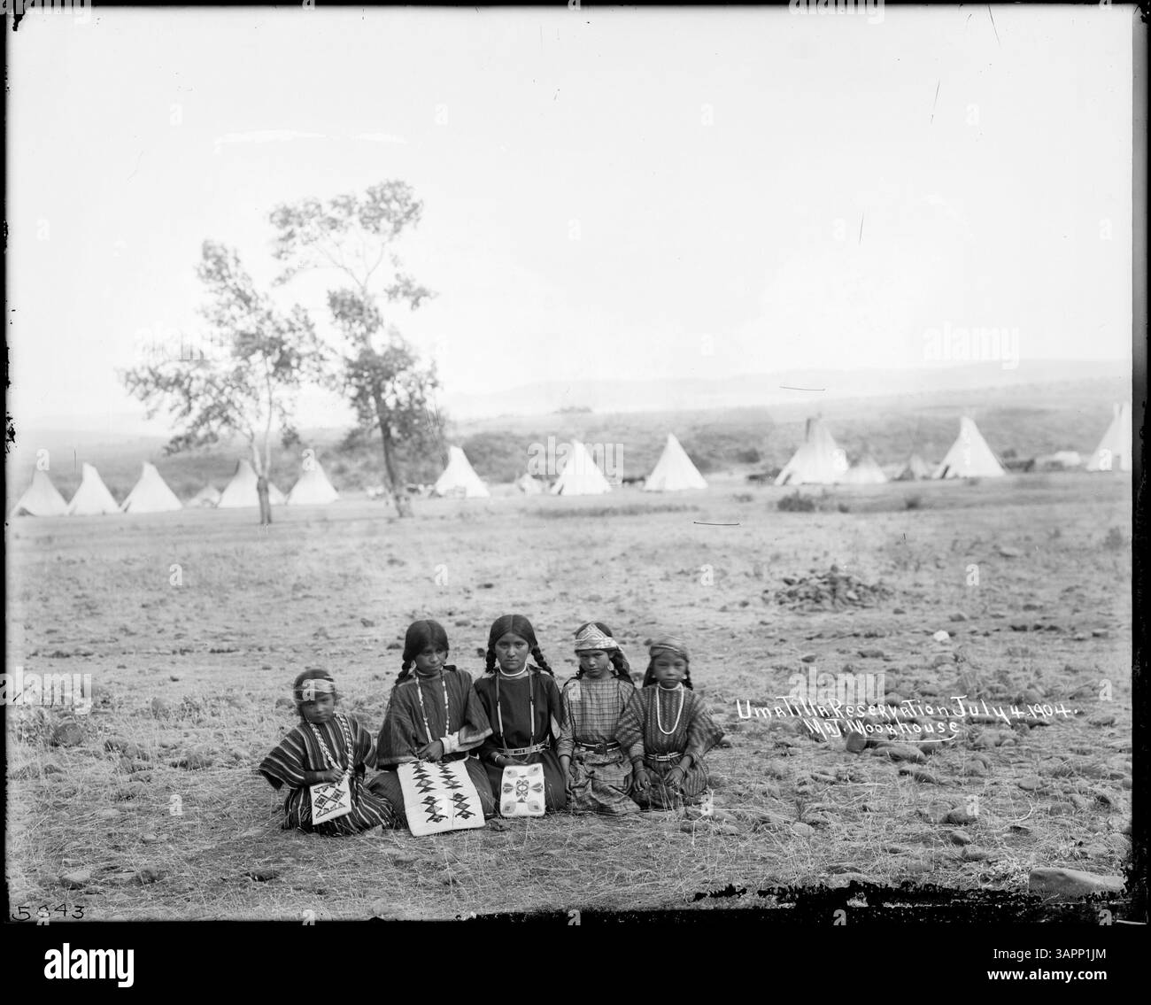 Dieses Schwarzweiß-Foto zeigt fünf indianische Mädchen, die auf dem Boden knieten, drei davon mit Perlen bestückte Taschen und Tipis im Hintergrund. Das Bild ist Teil der Lee Moorhouse Kollektion. Stockfoto