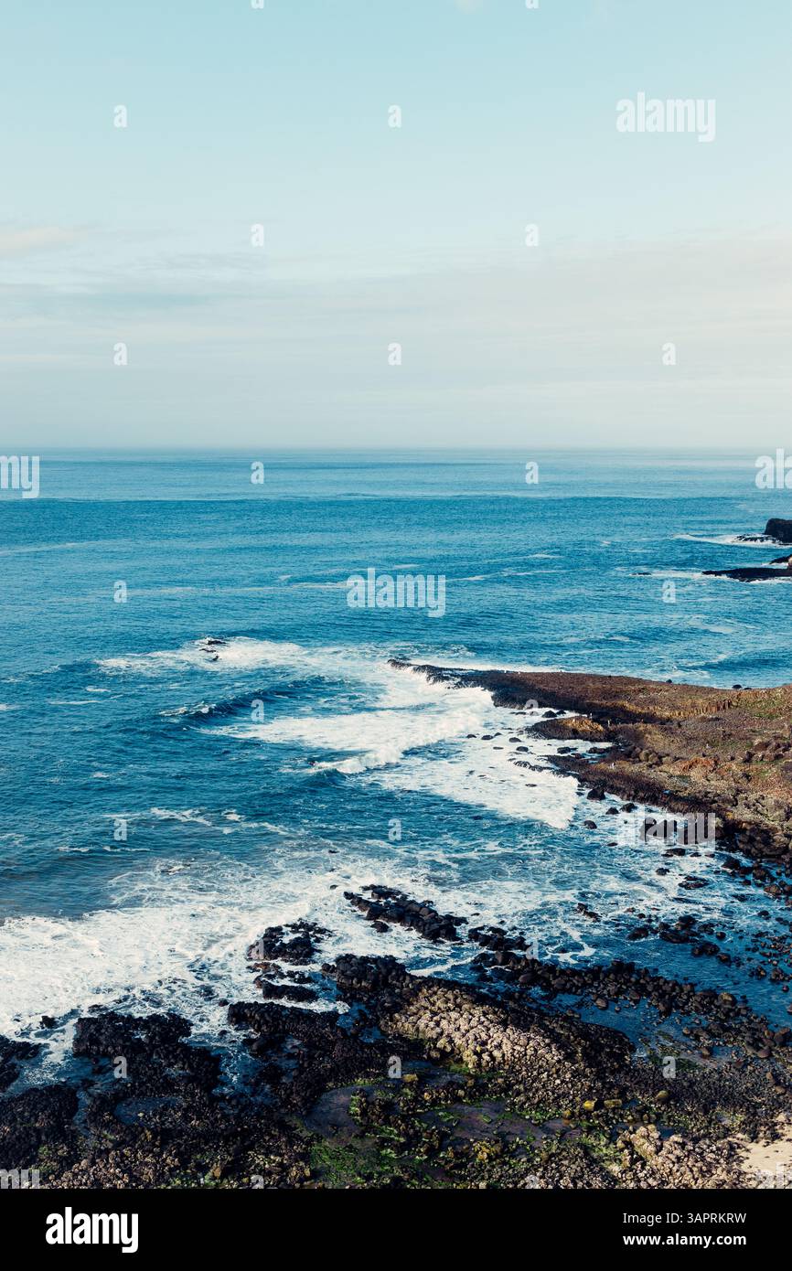 Moody Aerial View of Giant’s Causeway mit Wellen, die in die Felsen stürzen und Menschen herumlaufen Stockfoto