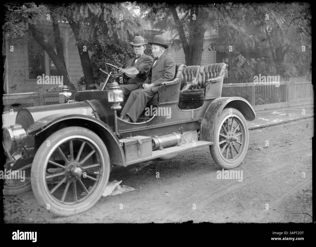 Foto von Lee Moorhouse von einer Autoparade in Pendleton, Oregon. Das Bild zeigt eine Nahaufnahme von zwei Männern in einem Auto, mit einem Haus im Hintergrund, das die Automobilkultur des frühen 20. Jahrhunderts zeigt. Stockfoto