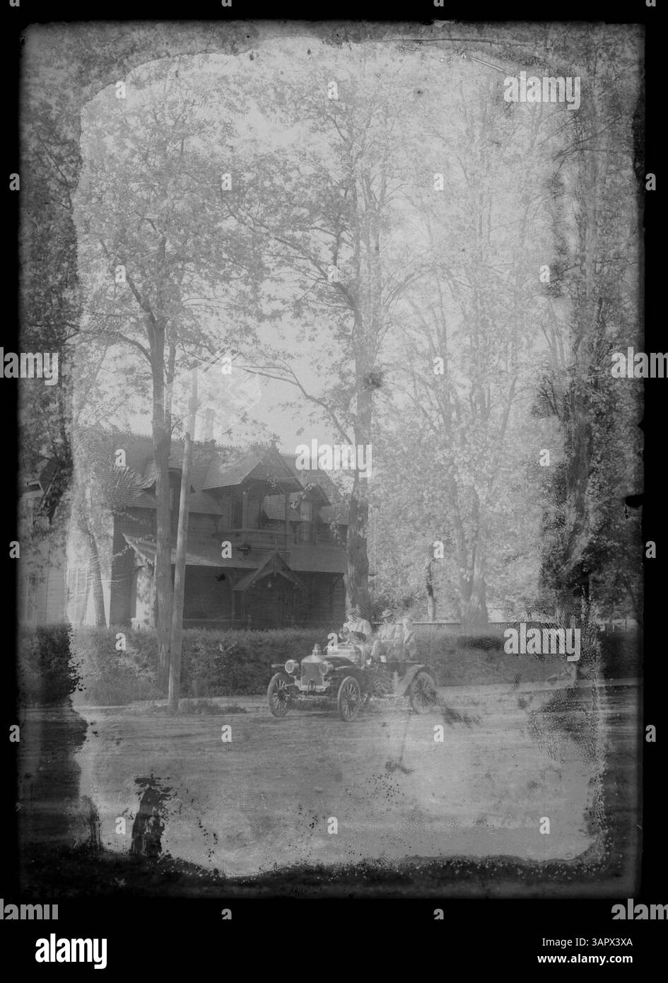 Dieses Foto von Lee Moorhouse zeigt ein Ford Model A Automobil, das auf einer Wohnstraße vor einem großen Haus geparkt ist. Das Bild spiegelt das amerikanische Vorstadtleben des frühen 20. Jahrhunderts und den Aufstieg der Automobilkultur wider. Stockfoto