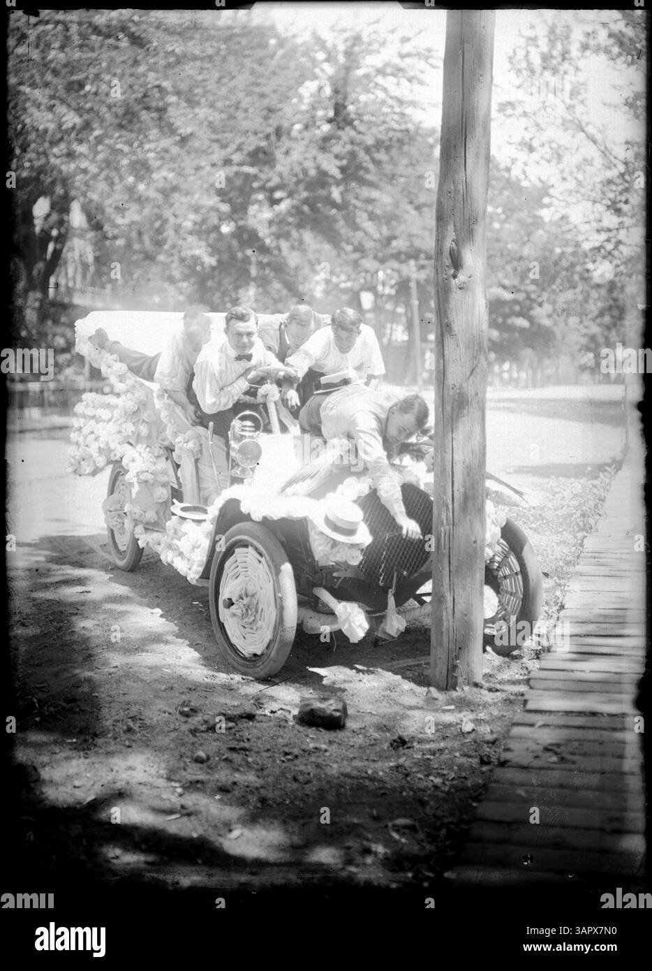 Dieses Foto zeigt eine Autoparade in Pendleton, Oregon. Fünf Männer in einem Auto sehen sich scherzhaft an, als ob das Fahrzeug gegen einen Baum gestürzt ist. Das Auto ist mit Baumwoll- oder weißen Rosetten dekoriert, was den unbeschwerten Charakter der Szene unterstreicht. Stockfoto