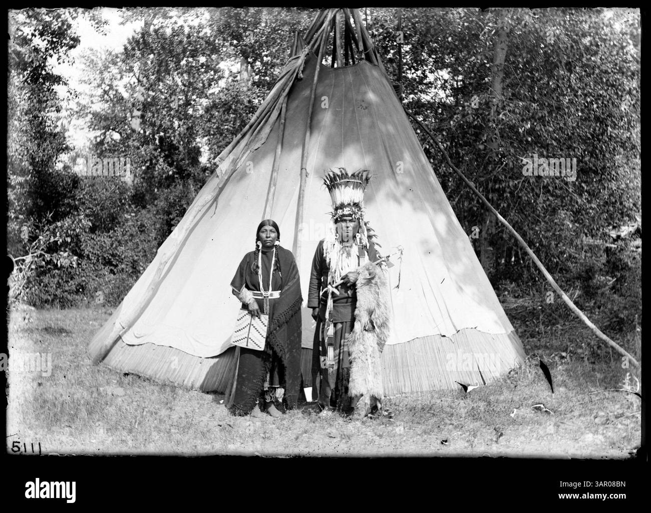 Dieses Foto zeigt Stammesmenschen, möglicherweise Yakimas, die in Regalia gekleidet sind und bei Tipis stehen. Es ist Teil der Lee Moorhouse Kollektion und zeigt das kulturelle Leben der indianischen Ureinwohner und traditionelle Wohnhäuser. Stockfoto