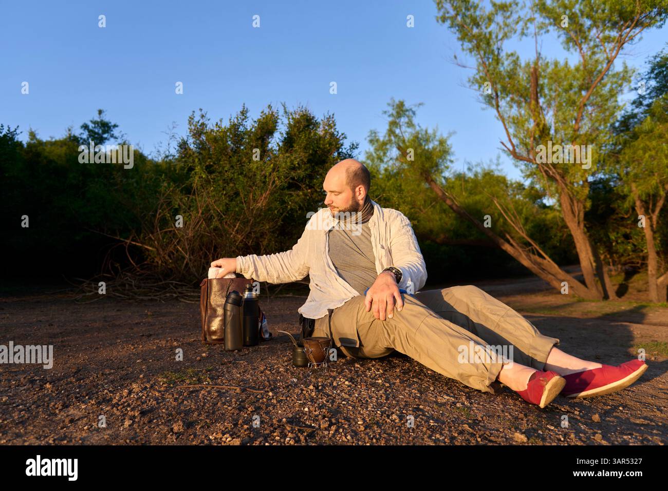 Hispanischer Reisender, der bei Sonnenaufgang am Ufer eines Baches sitzt, entspannt und die ersten Sonnenstrahlen empfängt. El Palmar Nationalpark, Entre Rios, Ar Stockfoto