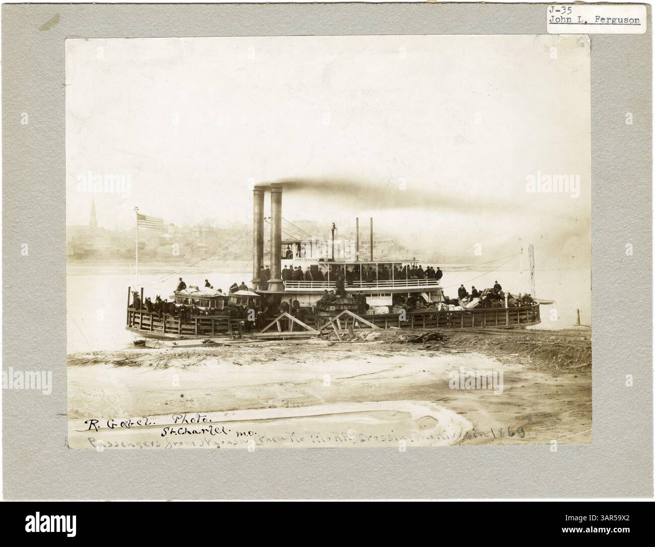 Dieses Schwarzweiß-Foto zeigt das Dampfschiff John L. Ferguson, das 1869 am Missouri River angedockt hat. Die Passagiere sind auf dem oberen Deck zu sehen, während sich die Fracht auf dem Hauptdeck befindet. Stockfoto