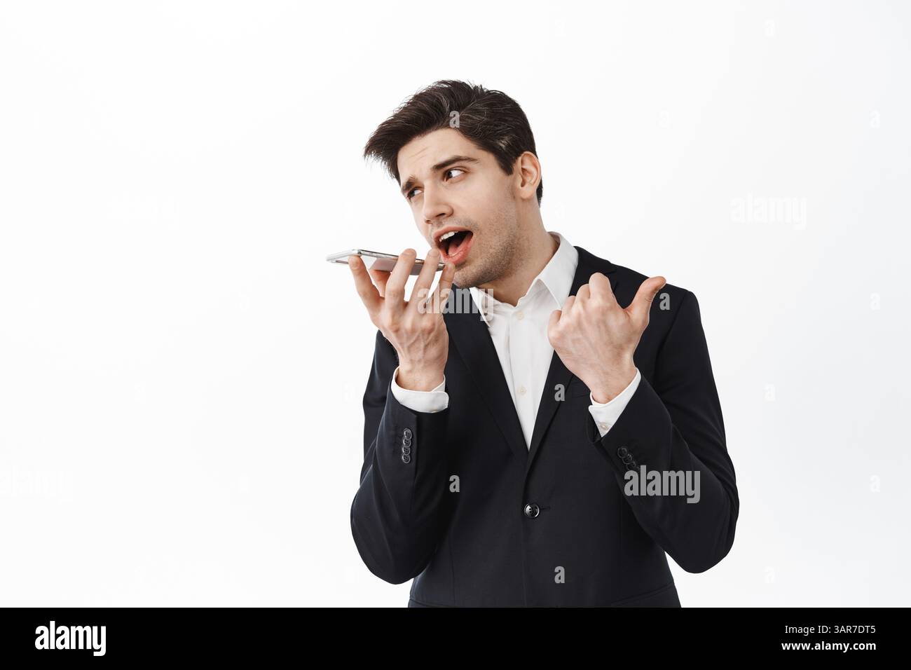 Firmenmann, der über Freisprecheinrichtung spricht und auf den Fingern zählt, gibt während des Telefonanrufs Anweisungen und steht mit dem Smartphone vor weißem Hintergrund. Stockfoto