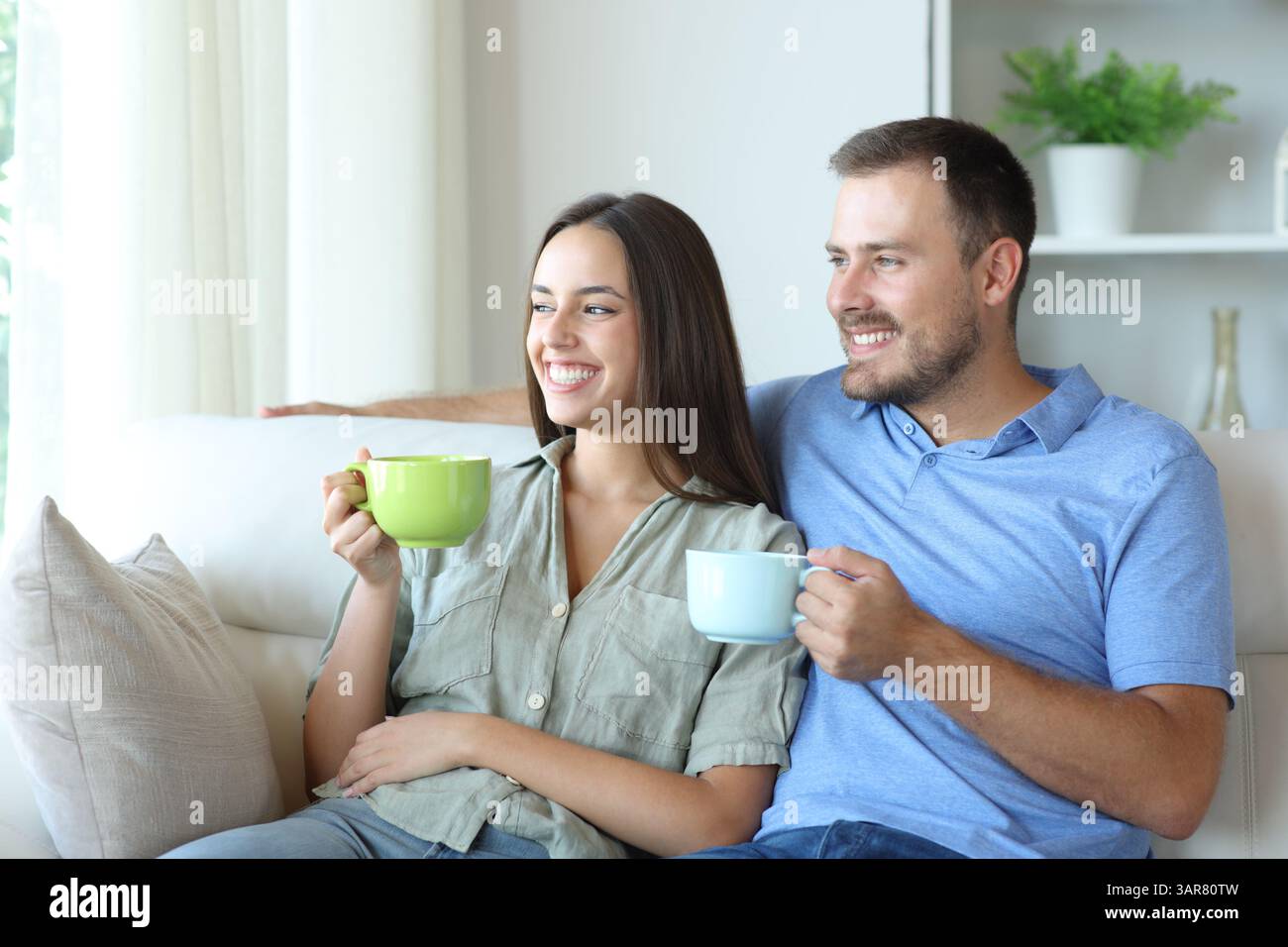 Glückliches Paar, das sich auf einem Sofa entspannt und zu Hause Tee trinkt Stockfoto