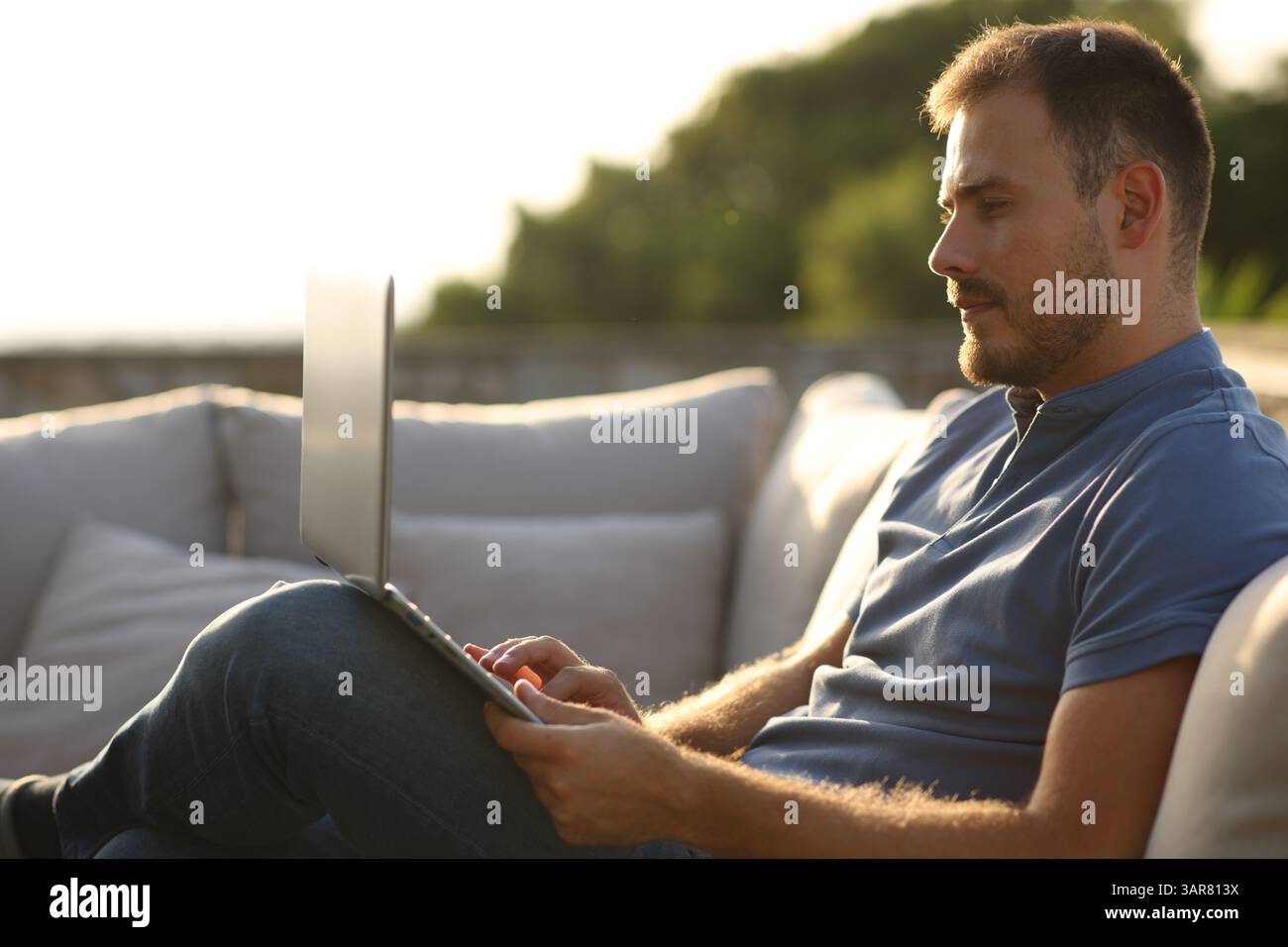Ernsthafter Mann, der einen Laptop benutzt und auf einer Terrasse zu Hause oder im Hotel sitzt Stockfoto
