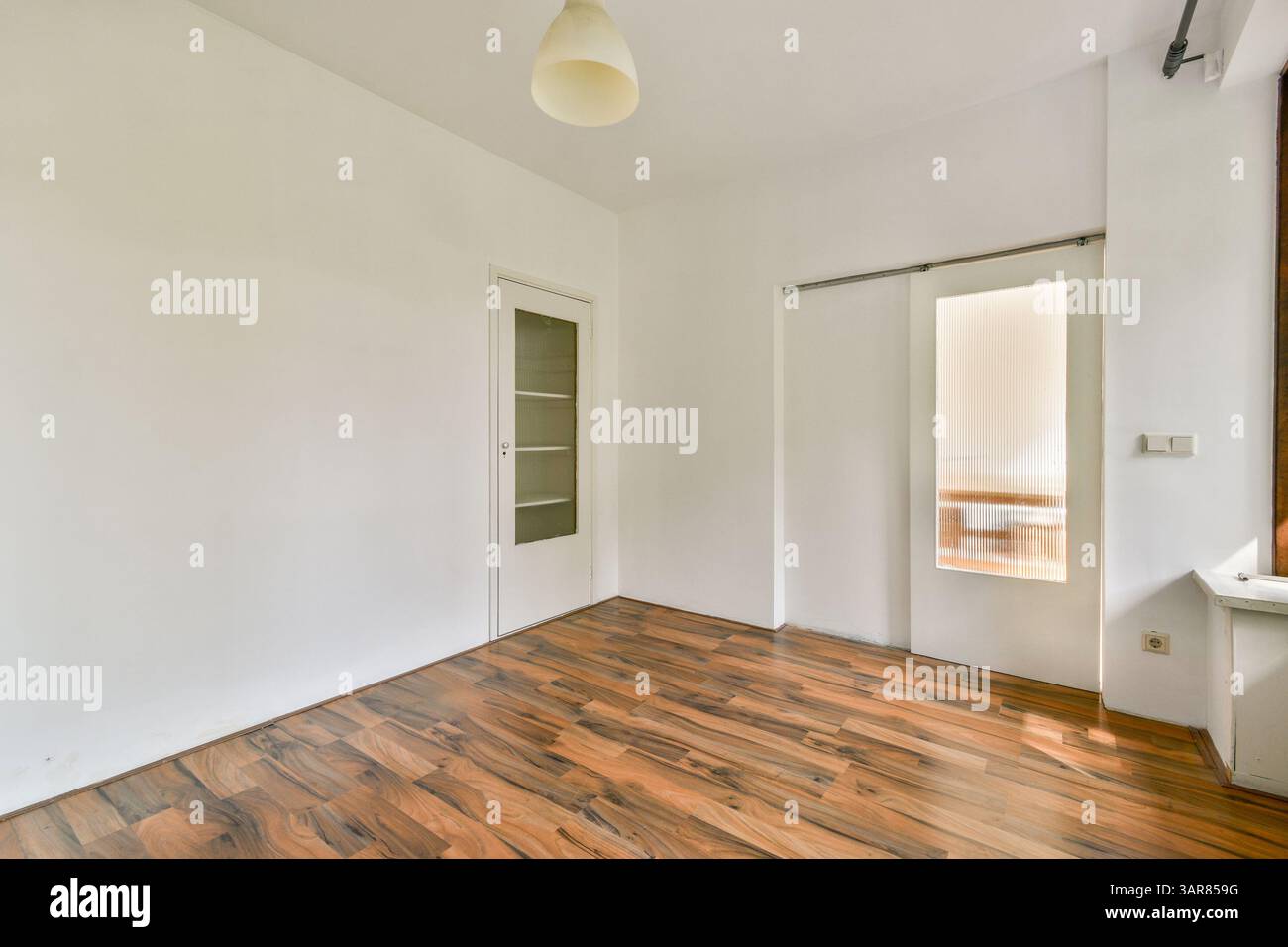 Die geräumige, minimalistische Inneneinrichtung ist mit Holzfußboden und einfachen weißen Wänden ausgestattet. Der Raum ist gut beleuchtet und verfügt über Tageslicht und eine saubere, übersichtliche Atmosphäre. Stockfoto