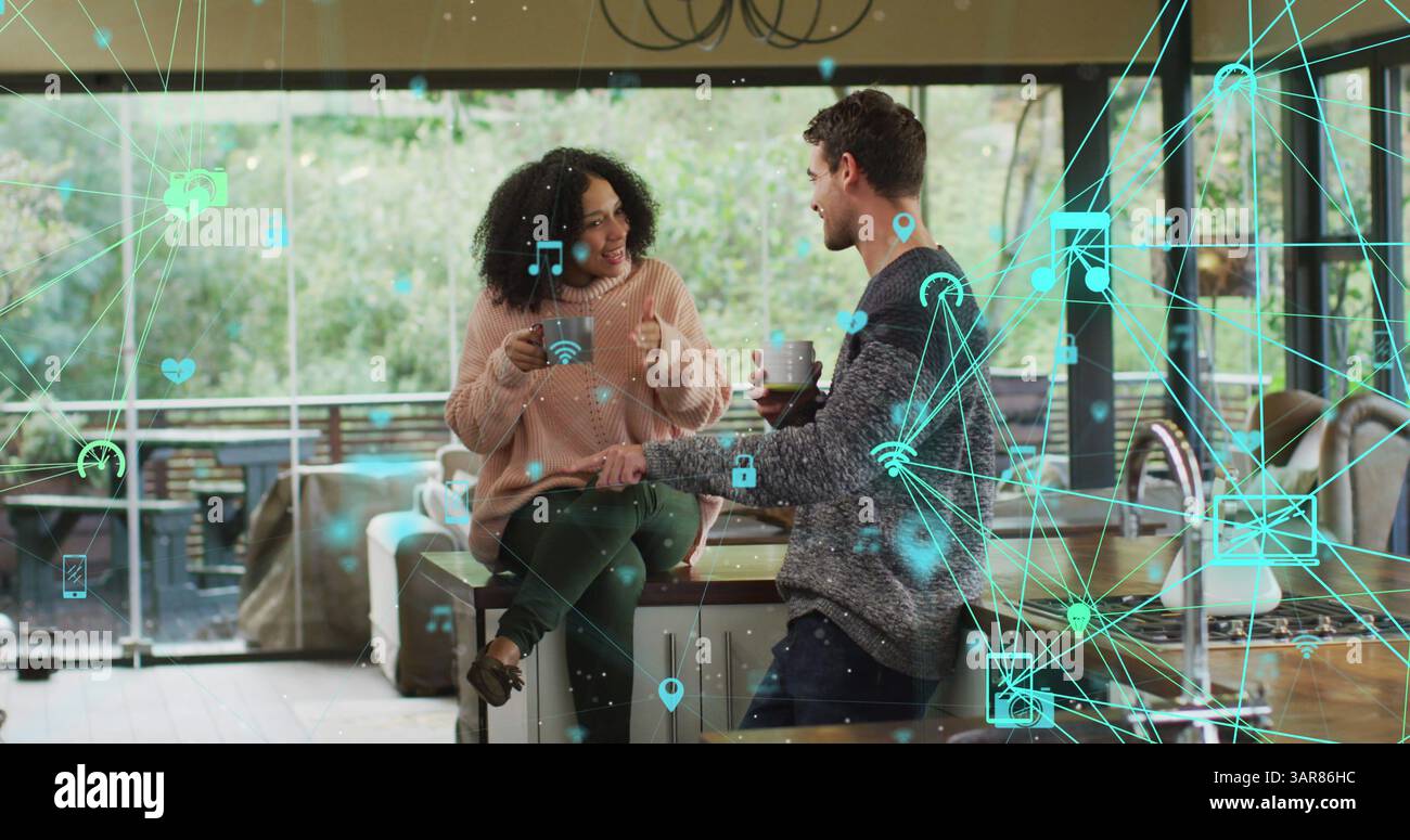 Bild eines Netzwerkes von Mediensymbolen über glückliche, birassische Paare, die zu Hause Kaffee trinken Stockfoto