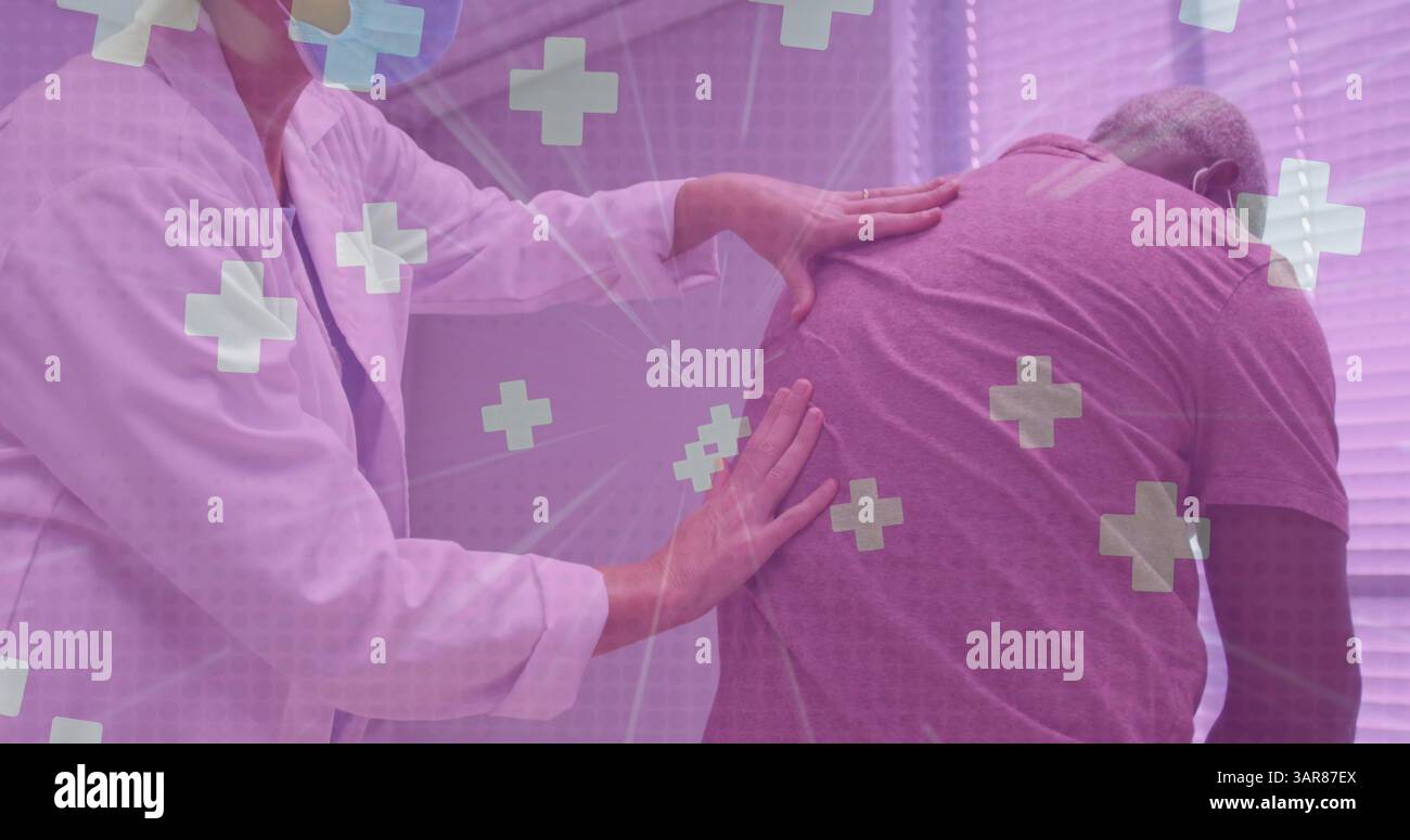 Mehrere medizinische Symbole schweben gegen Arzt, der den Rücken eines älteren Mannes im Krankenhaus untersucht Stockfoto