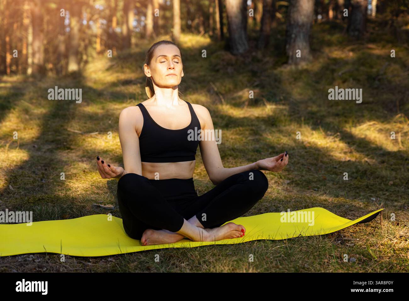 Frau übt Yoga-Übungen und Meditation auf Matte in einem sonnigen Wald. Genießen Sie die Schönheit von Achtsamkeit und Natur Stockfoto