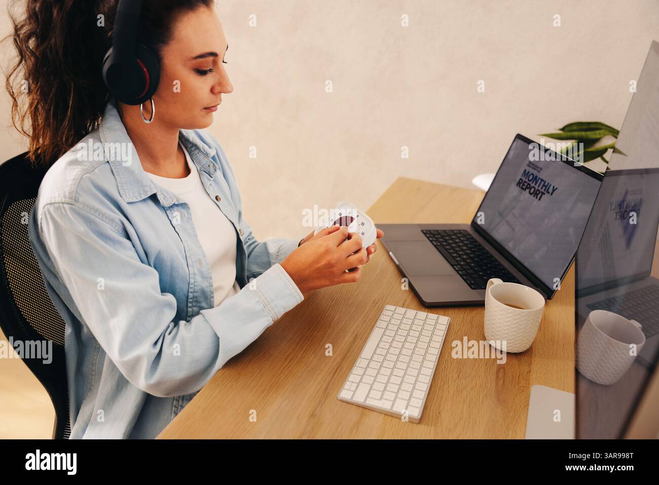 Junge Frau, die sich auf Produktivität konzentriert, Kopfhörer trägt, einen Timer während der Arbeit am Schreibtisch verwendet. Das Bild vermittelt Themen der Konzentration, des Zeitmanagements Stockfoto