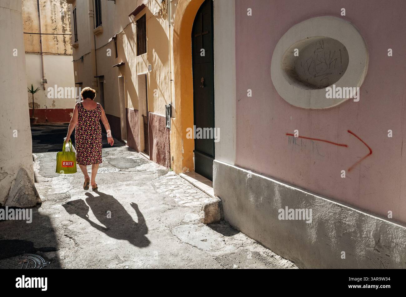 Frau gefolgt von ihrem Schatten in einer Gasse, Gallipoli, Salento, Apulien, Italien Stockfoto