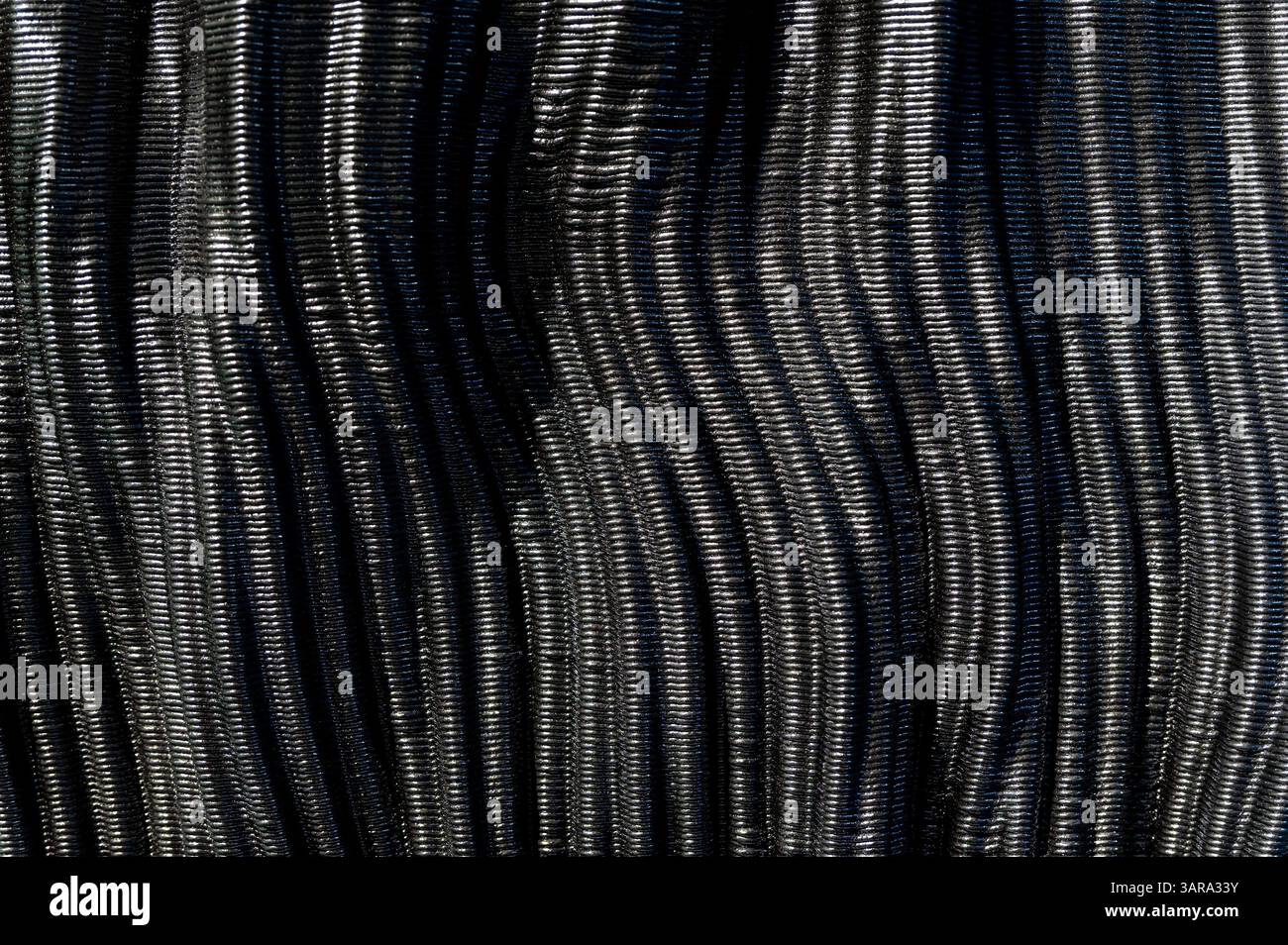Nahaufnahme der welligen Textur glänzender schwarzer Kohlefaser, die einen eleganten und futuristischen Hintergrund schafft Stockfoto