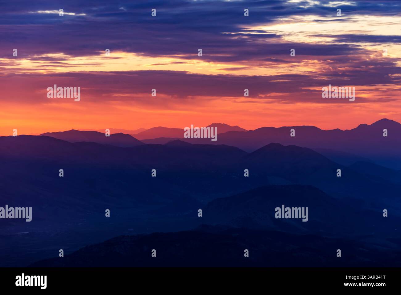 Ein atemberaubender Blick auf die geschichteten Berge während des Sonnenuntergangs mit einem Farbverlauf von Orange bis Lila am Himmel. Die Silhouette des Berges Stockfoto