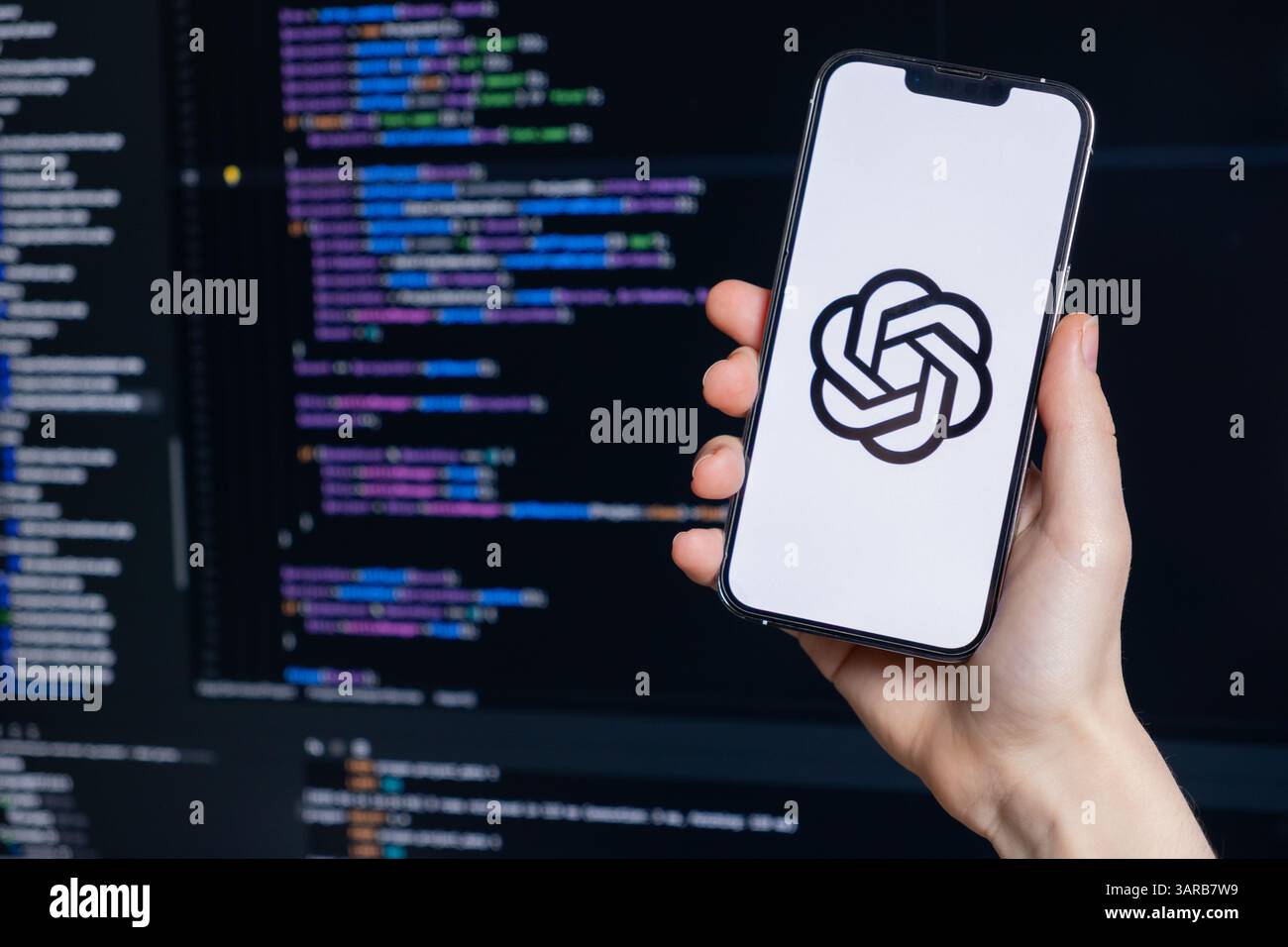 Poznan, Polen – 14. April 2025: Das ChatGPT-Logo wird auf dem Smartphone angezeigt, das vom Entwickler vor dem Code-Editor gehalten wird und die KI-Nutzung in moderner Software veranschaulicht Stockfoto