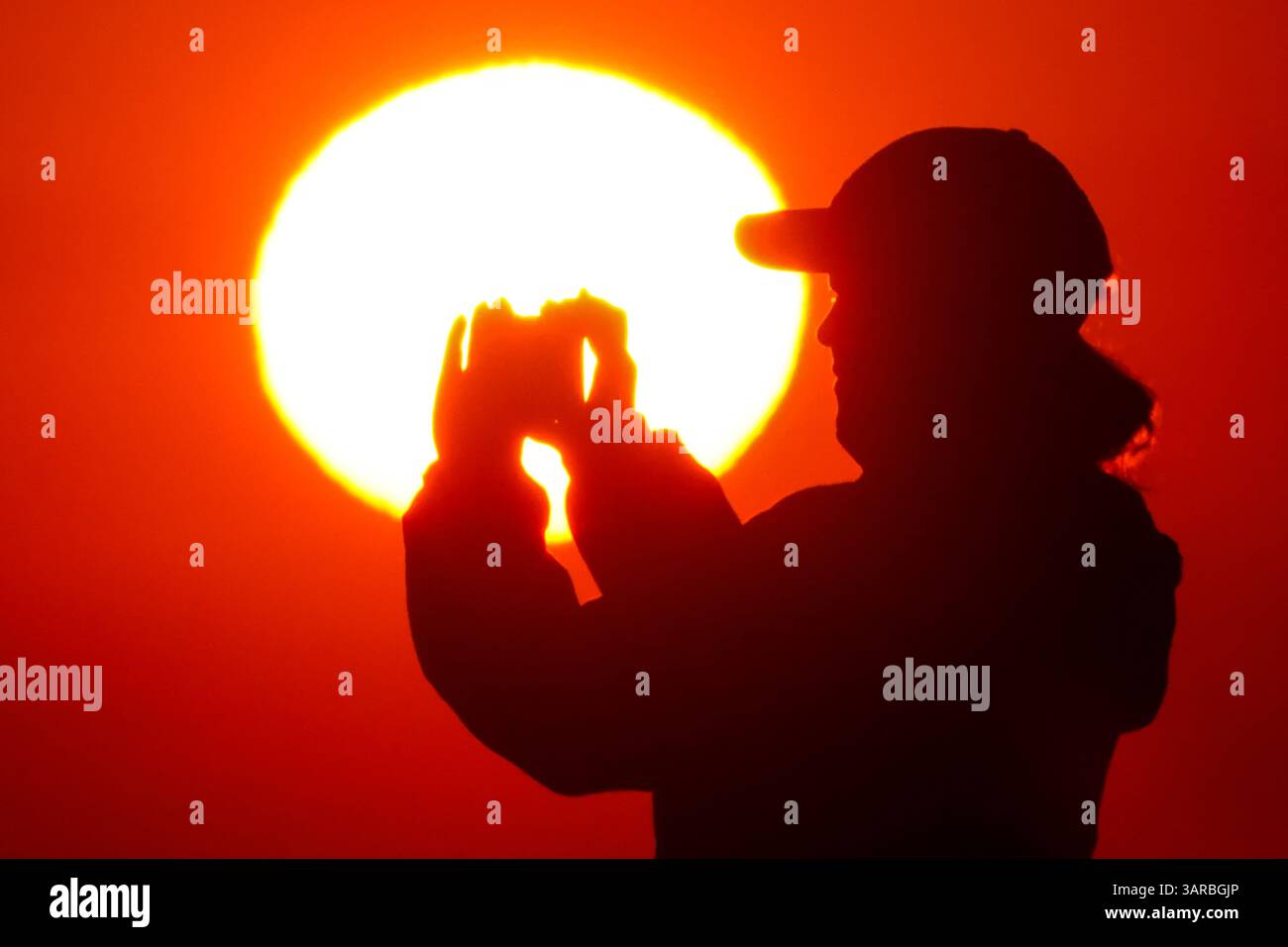 Isle Of Palms, Usa. April 2025. Ein Fotograf mit der Silhouette des Sonnenaufgangs macht Fotos, während die Sonne am Strand des Wild Dunes Resort am 17. April 2025 in Isle of Palms, South Carolina, über den Horizont steigt. Quelle: Richard Ellis/Richard Ellis/Alamy Live News Stockfoto