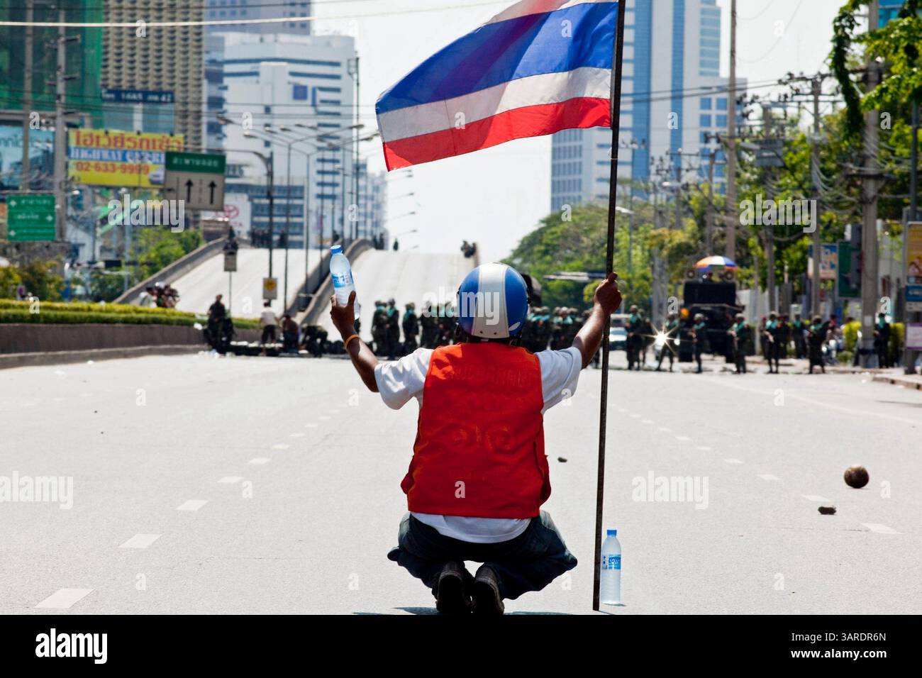 14. Mai 2010 - Bangkok, Thailand - ein regierungsfeindlicher Demonstrant bietet thailändischen Truppen Wasser an, während er die thailändische Flagge auf der Rama IV Rd. Schwenkt Die thailändischen Sicherheitskräfte haben Live-Patronen abgefeuert, nachdem sie ein schwer verteidigtes Demonstrantenlager in Bangkok wegen Zusammenstößen, bei denen zwei Menschen getötet wurden, versiegeln wollten. Botschaften wurden geschlossen, als Demonstranten einen Polizeibus in Brand setzten und Feuerwerke auf Truppen schossen, die auch mit Tränengas und Gummigeschossen reagierten. Die Demonstranten wollen, dass der Premierminister zurücktritt und Wahlen ausruft. Viele der sogenannten Red-Shirt-Demonstranten unterstützen den ehemaligen Premierminister Thaksin Shinawatra, Stockfoto