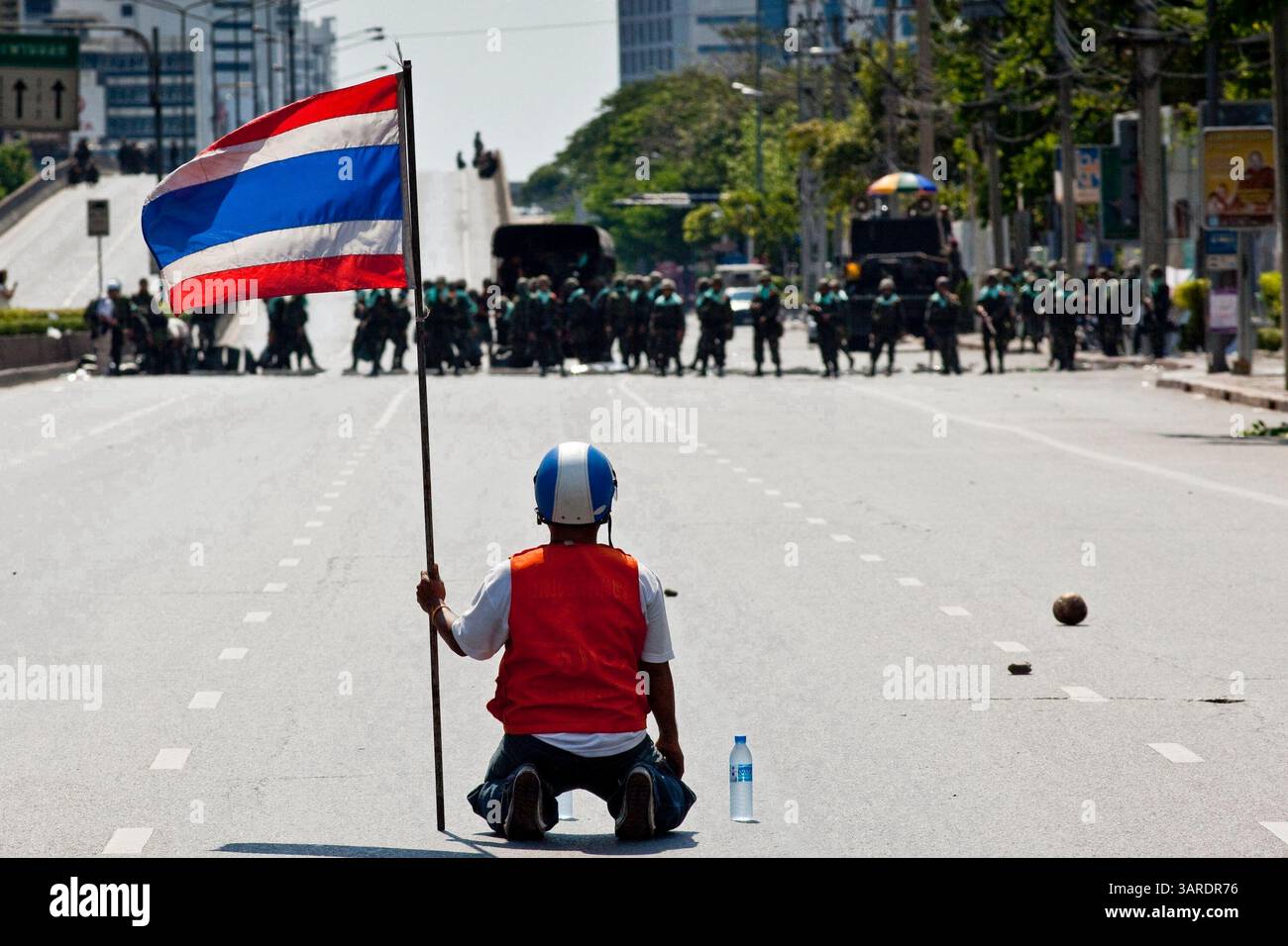 14. Mai 2010 - Bangkok, Thailand - ein regierungsfeindlicher Demonstrant bietet thailändischen Truppen Wasser an, während er die thailändische Flagge auf der Rama IV Rd. Schwenkt Die thailändischen Sicherheitskräfte haben Live-Patronen abgefeuert, nachdem sie ein schwer verteidigtes Demonstrantenlager in Bangkok wegen Zusammenstößen, bei denen zwei Menschen getötet wurden, versiegeln wollten. Botschaften wurden geschlossen, als Demonstranten einen Polizeibus in Brand setzten und Feuerwerke auf Truppen schossen, die auch mit Tränengas und Gummigeschossen reagierten. Die Demonstranten wollen, dass der Premierminister zurücktritt und Wahlen ausruft. Viele der sogenannten Red-Shirt-Demonstranten unterstützen den ehemaligen Premierminister Thaksin Shinawatra, Stockfoto