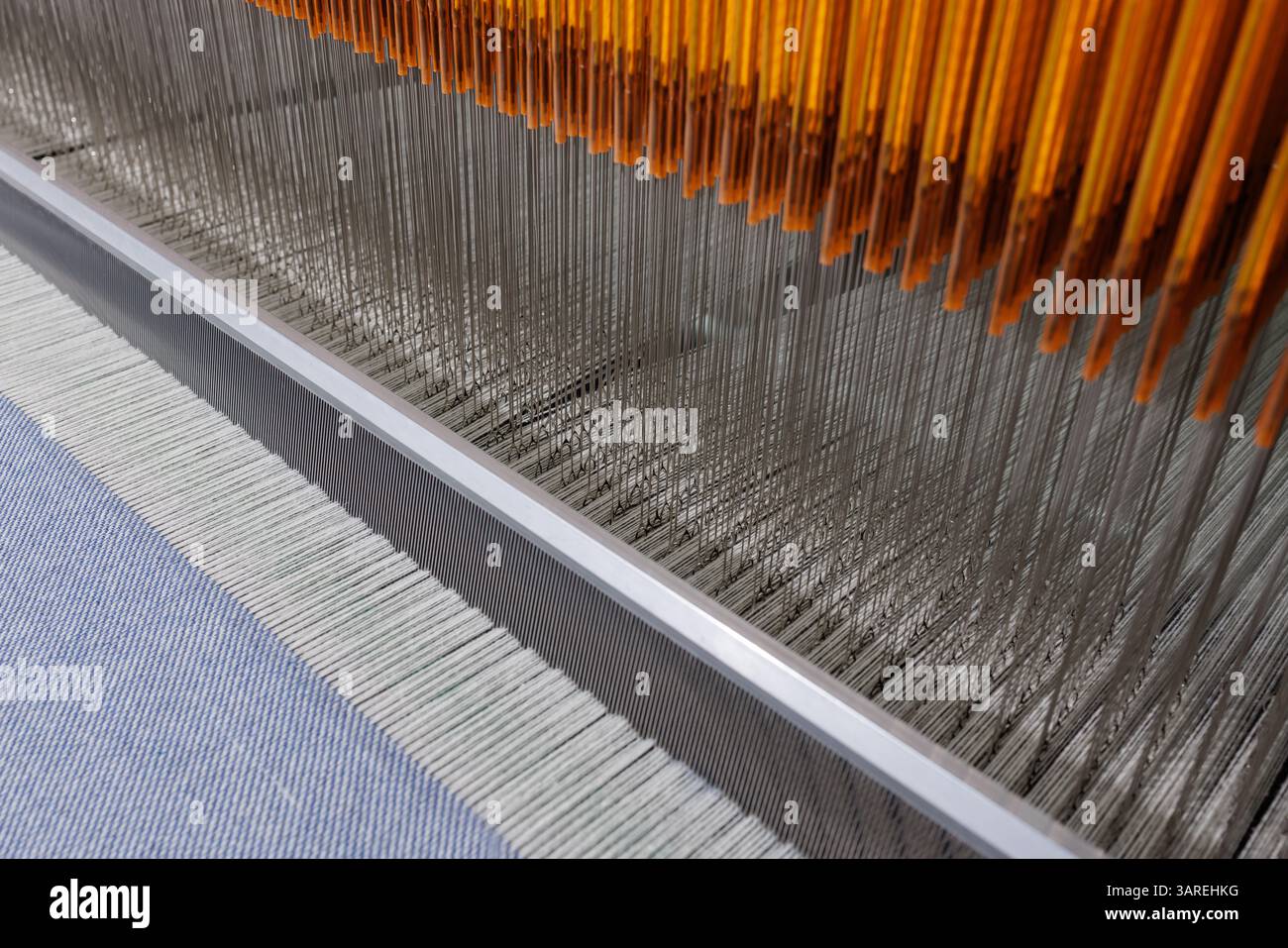 Nahaufnahme der industriellen Webmaschine mit ausgerichteten Fäden und Nadeln, Textilproduktion im Gange. Stockfoto